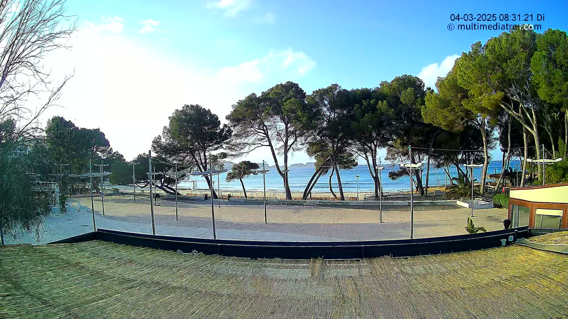 A paved plaza overlooks a sandy beach and calm ocean under a mostly sunny sky.
