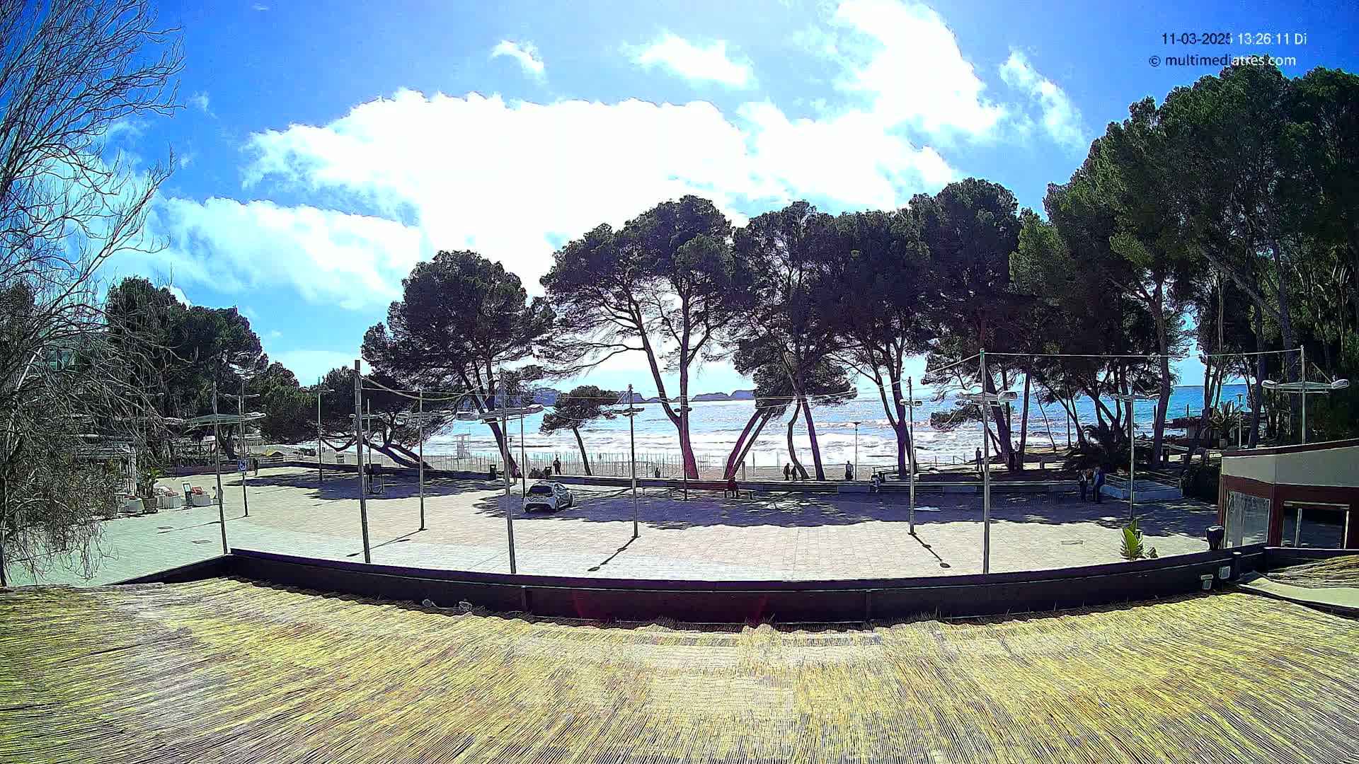 A paved plaza with a view of a beach and ocean under a partly cloudy blue sky.