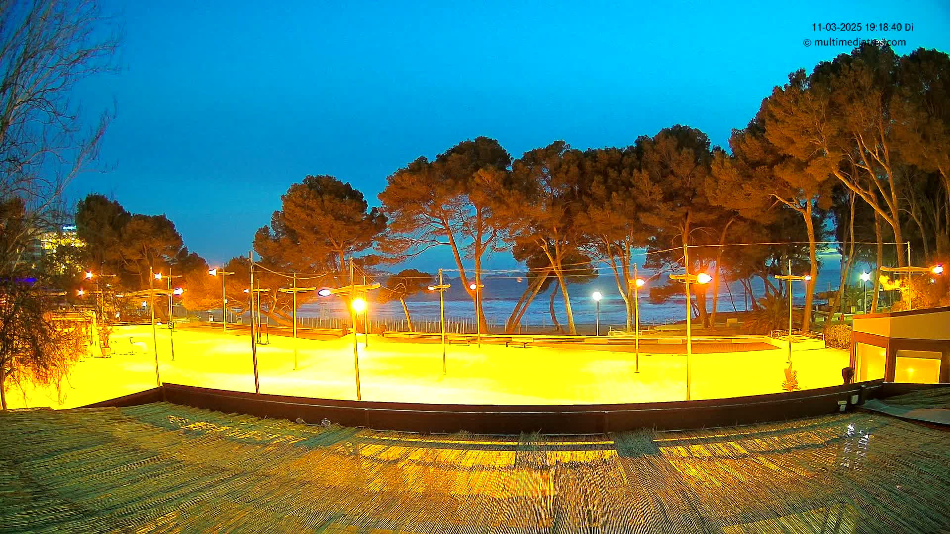 A brightly lit, empty outdoor rink sits near a beach under a twilight sky.