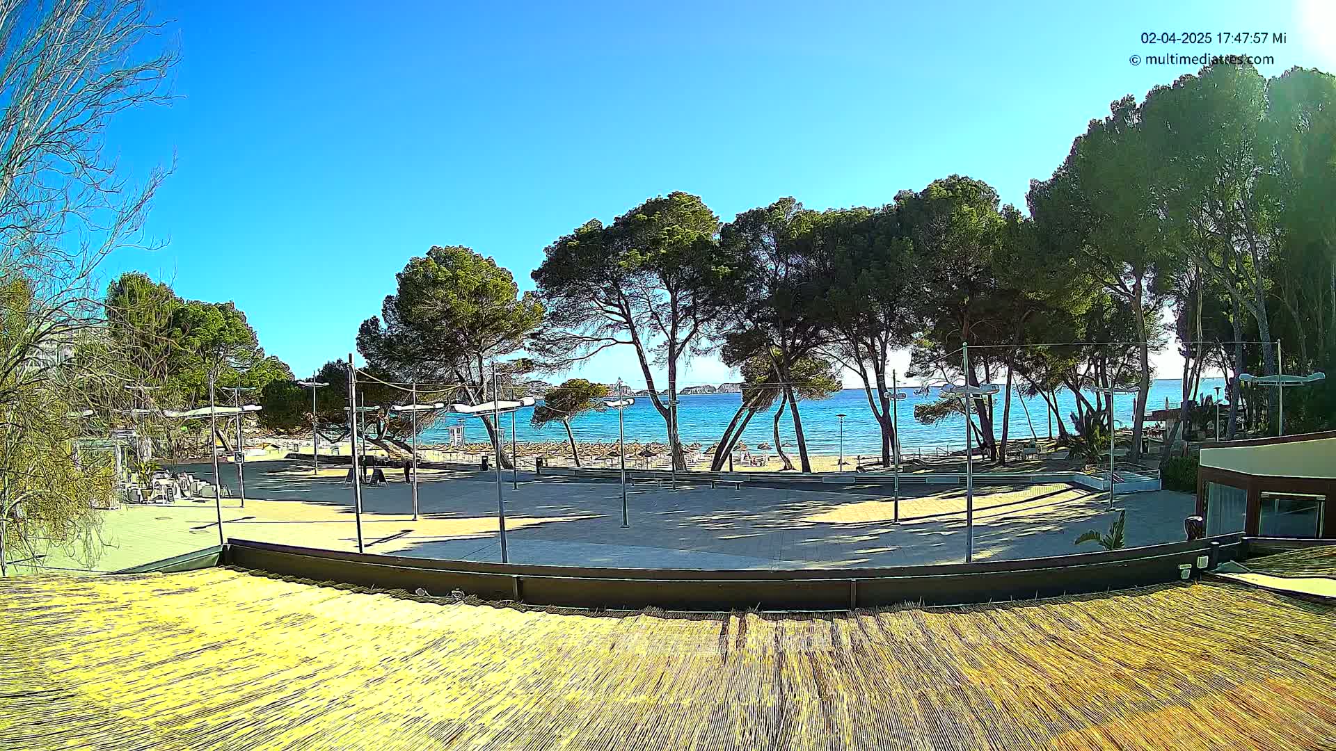 A paved outdoor area with a beach and clear blue ocean in the background under a sunny sky.