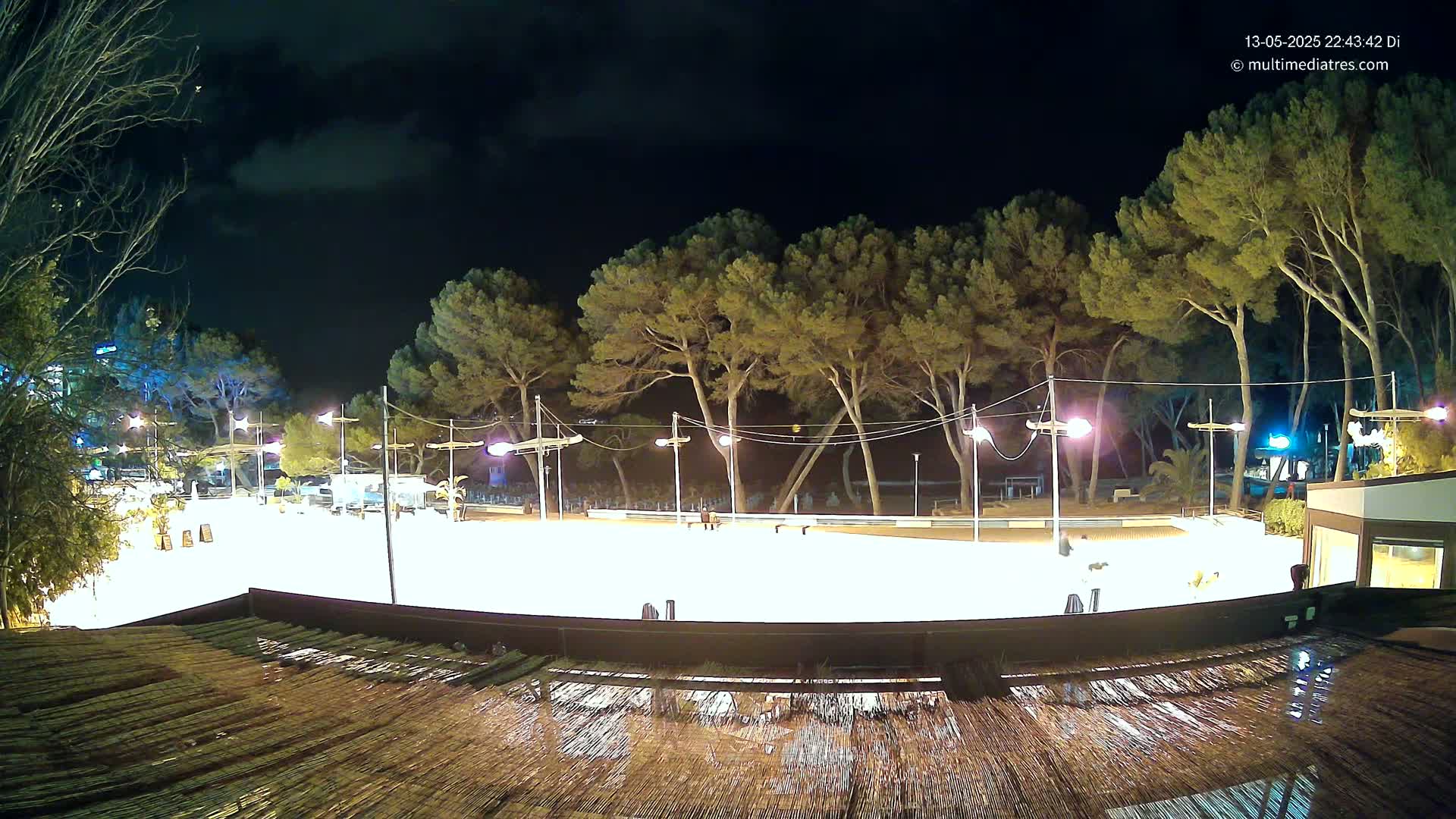 A brightly lit, empty outdoor skating rink at night, surrounded by trees under a partly cloudy sky.