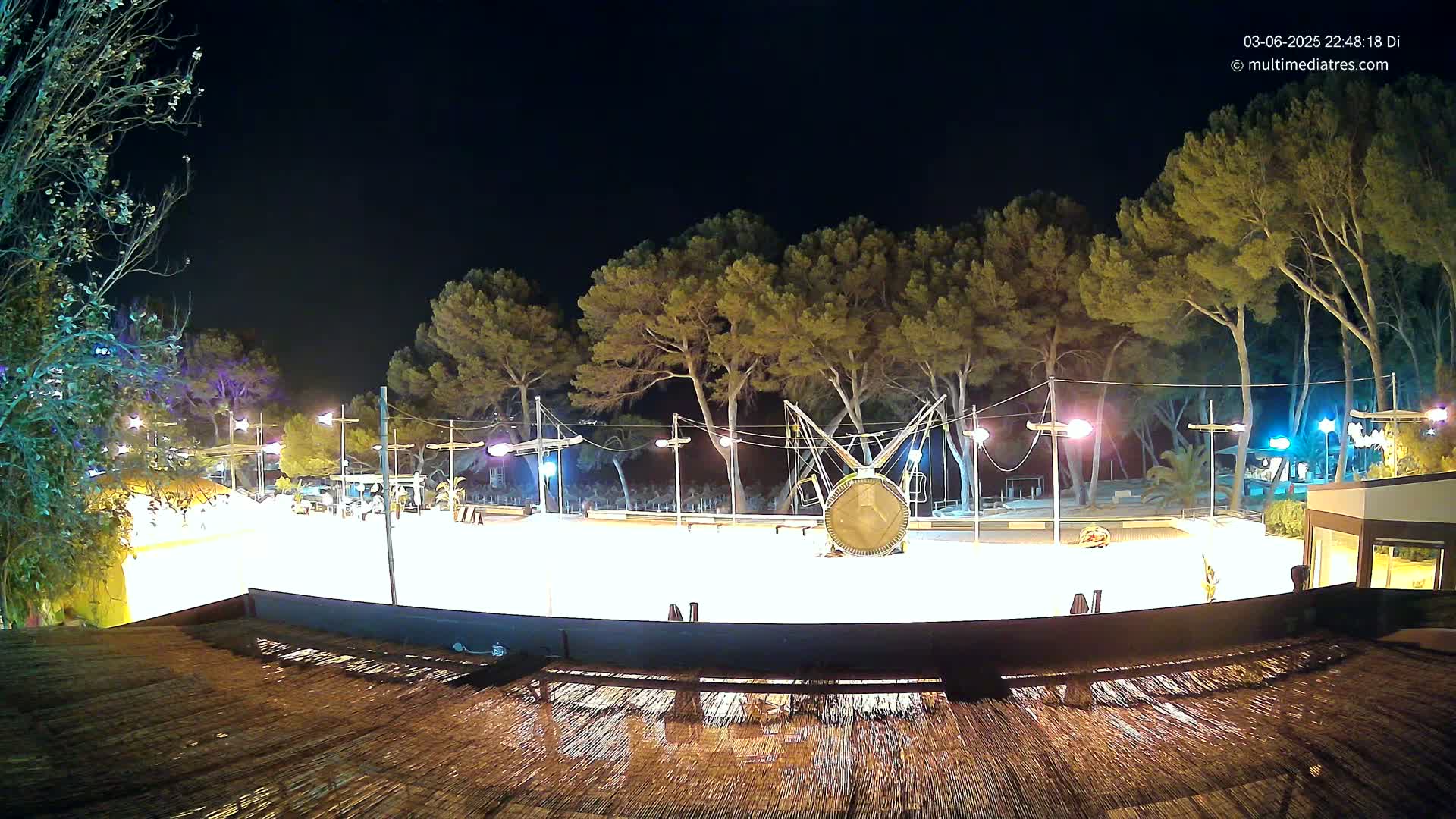 A brightly lit, outdoor skating rink at night, surrounded by trees and illuminated by lampposts.