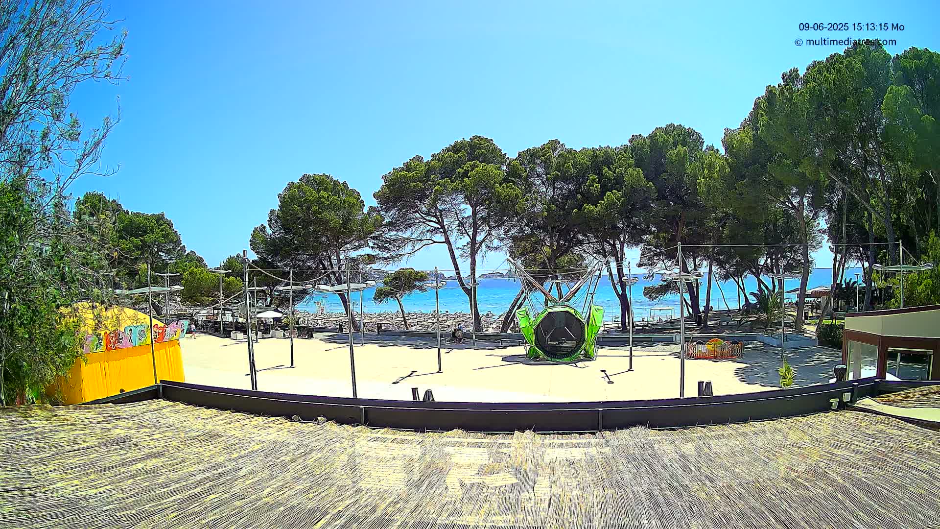 A sandy beachfront area with trees, a trampoline, and other recreational equipment is visible under a clear, sunny sky.