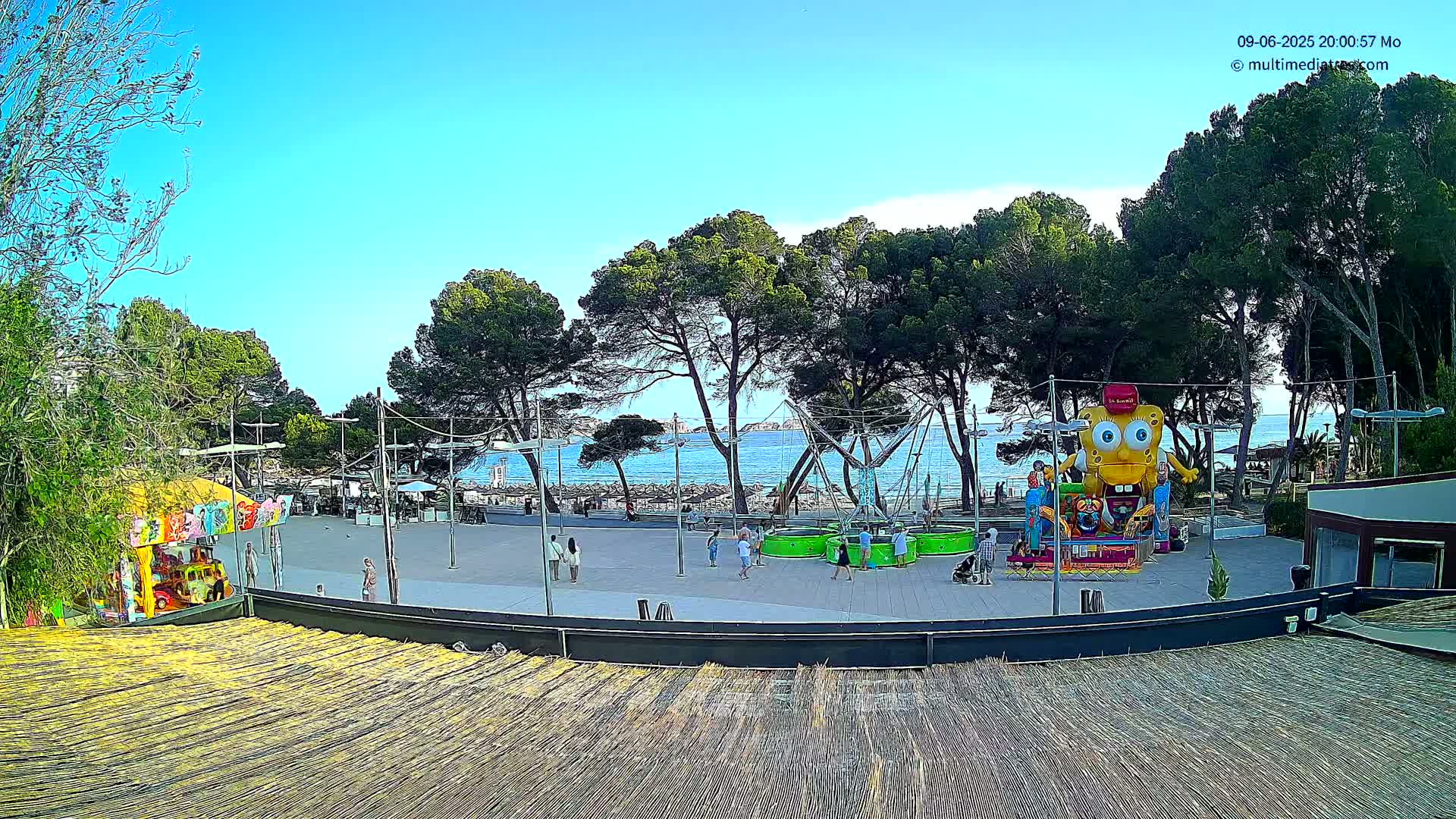 A seaside amusement area with rides and a beach in the background under a clear blue sky.