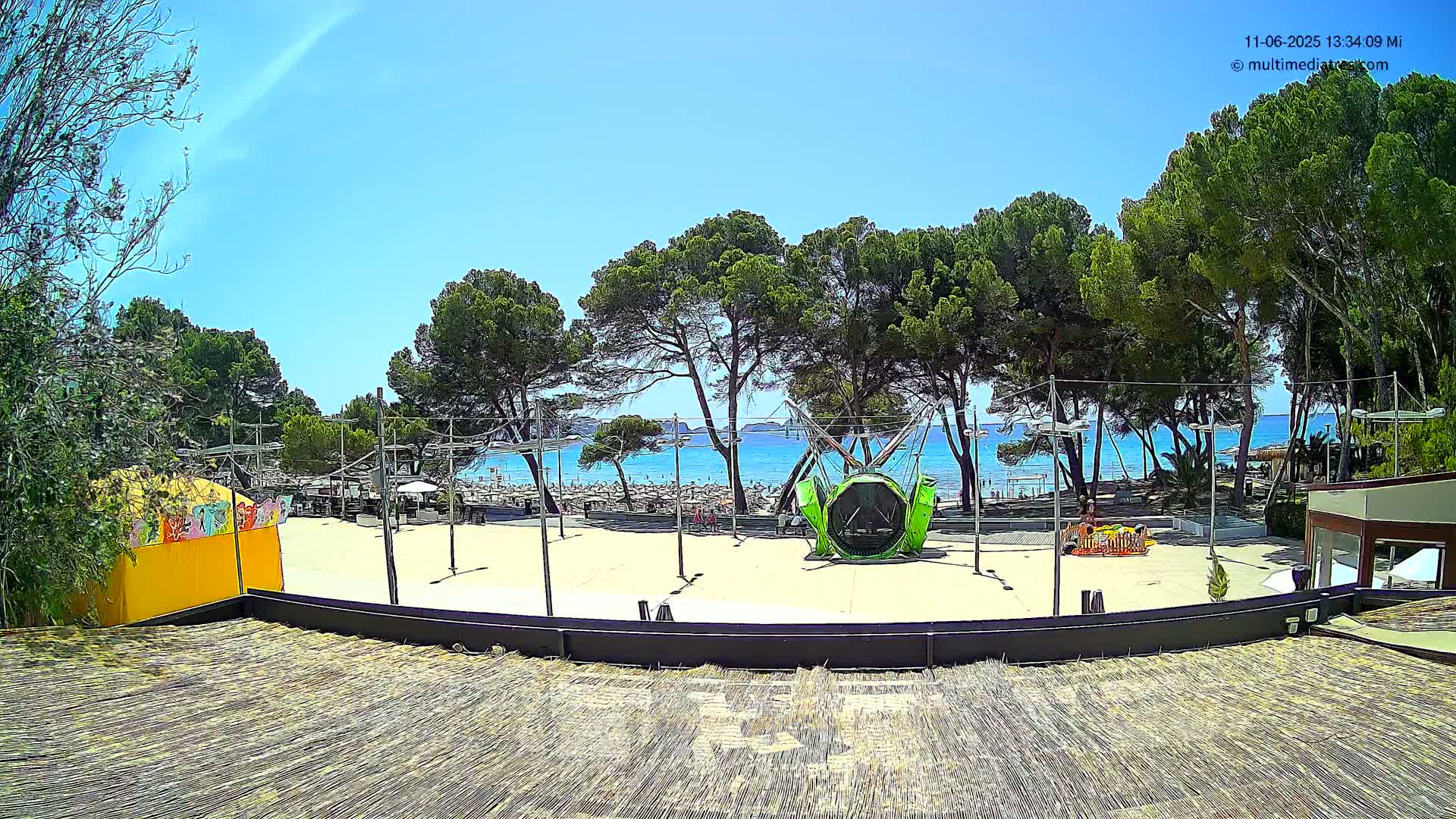 A sandy area with a playground and a beach in the background under sunny skies.