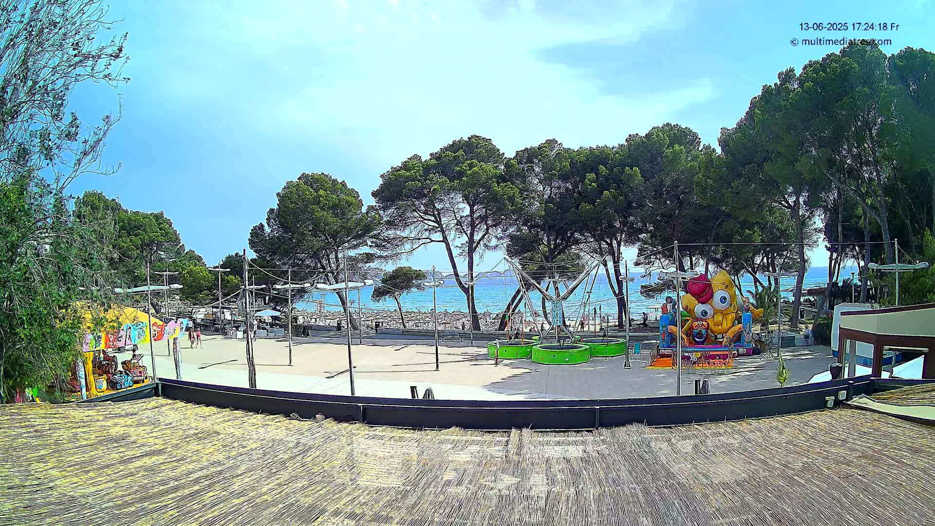 An outdoor amusement area with a bouncy attraction, near a beach on a sunny day.