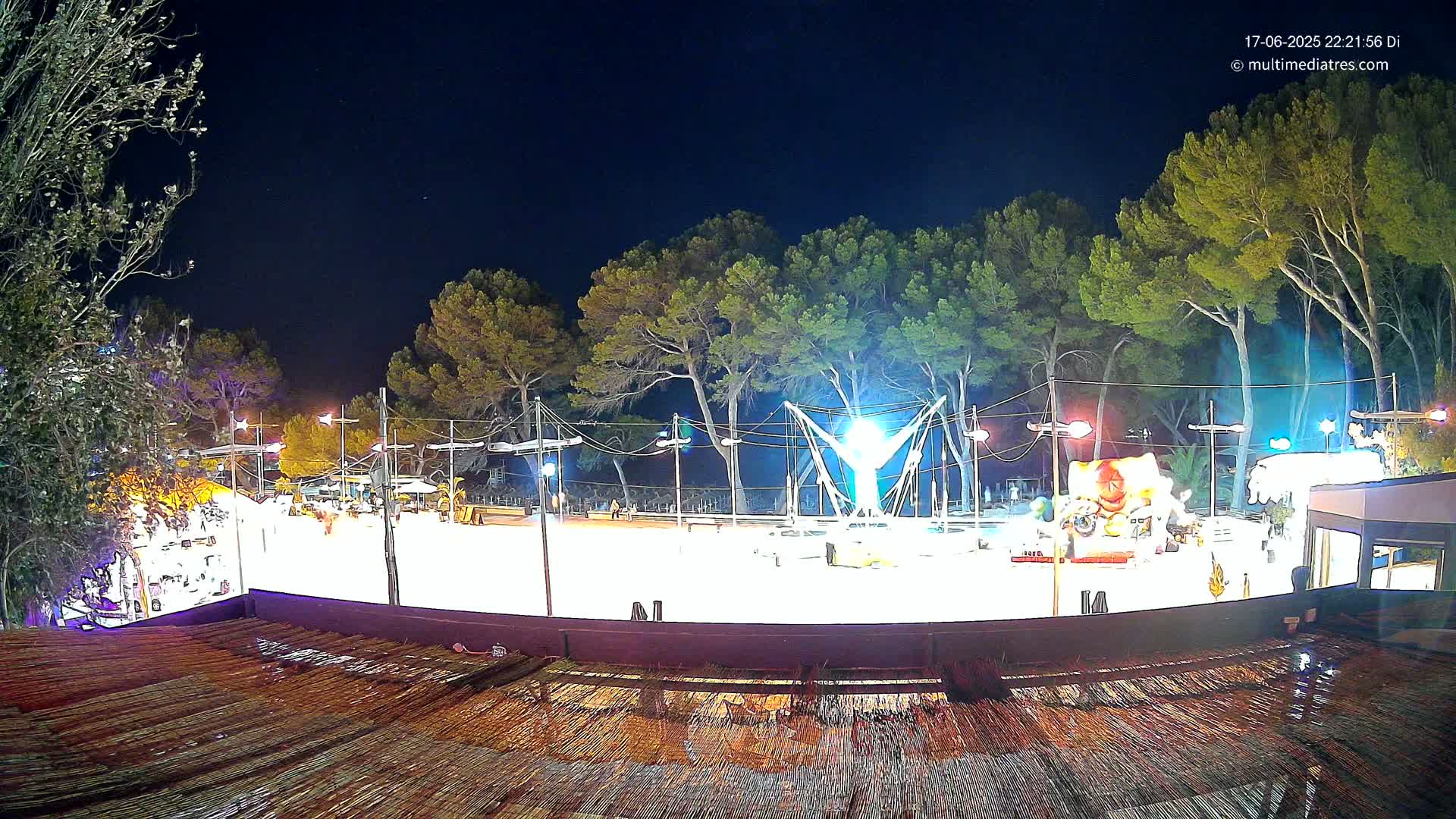 A brightly lit outdoor ice rink at night, surrounded by pine trees under a clear, dark sky.