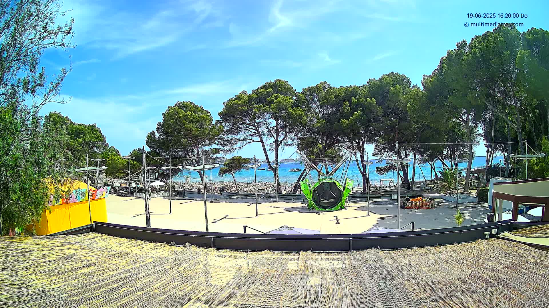 A sandy beach area with playground equipment, trees, and a building is visible, all under a sunny sky.