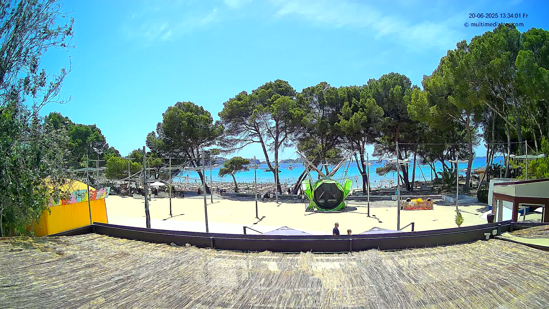 A sandy beach area with playground equipment and trees is visible, overlooking a calm blue ocean under a sunny sky.