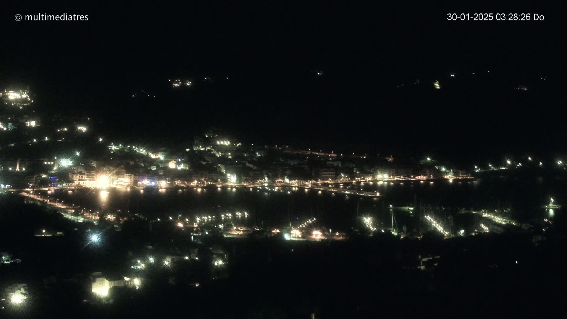 A nighttime, high-angle view of a coastal town illuminated by many lights surrounding a dark body of water.