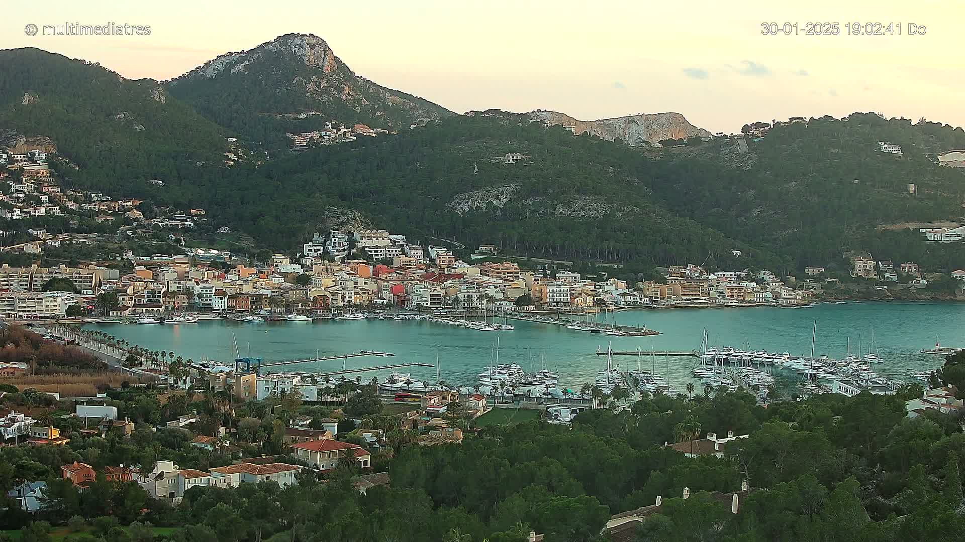A coastal town nestled in a bay, surrounded by verdant hills under a twilight sky.