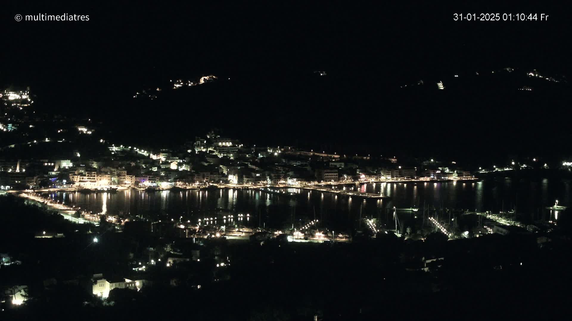 A nighttime view of a harbor town with its lights reflecting on the calm water.