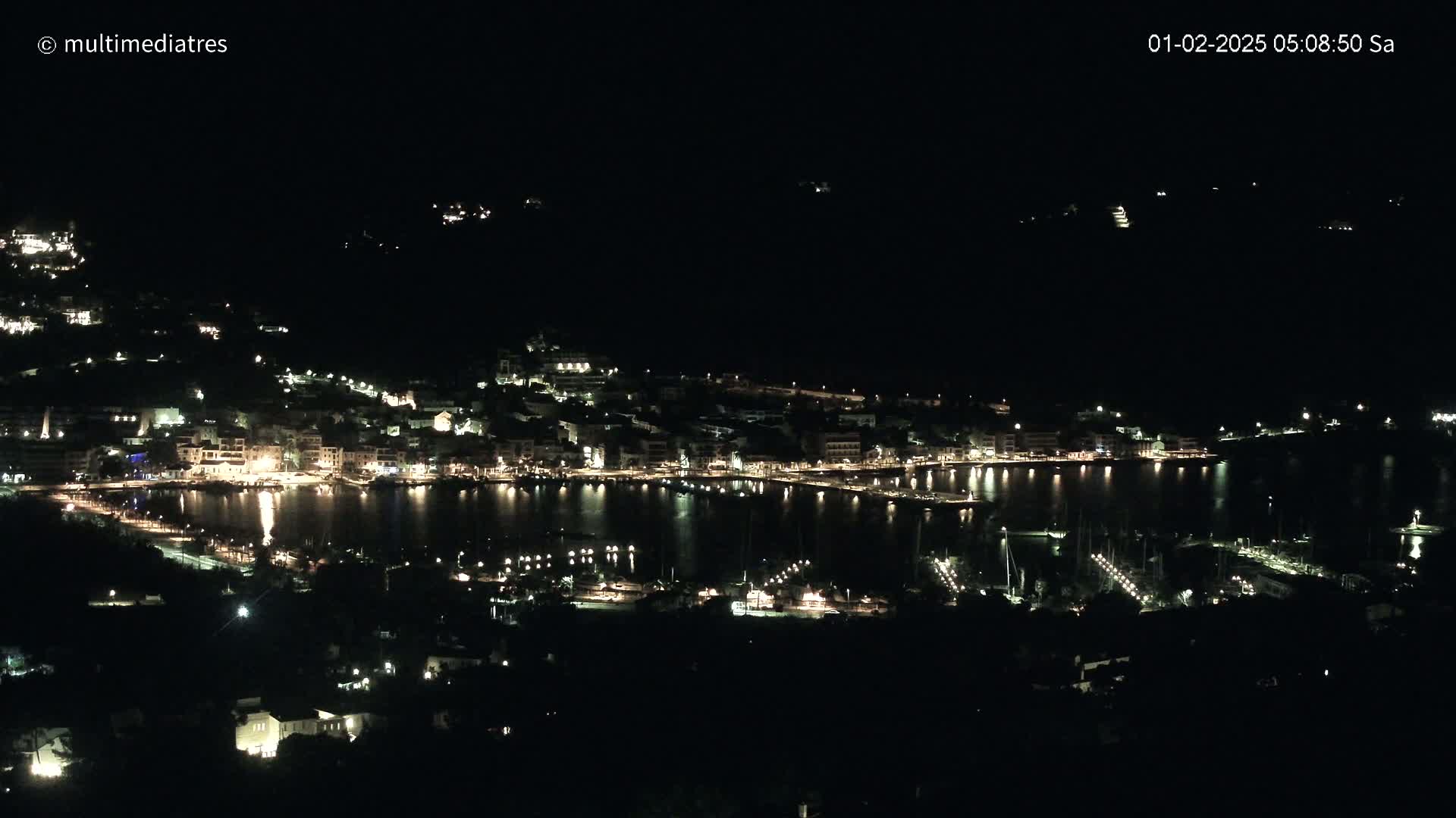 A nighttime view of a harbor town illuminated by lights, with calm water reflecting the lights.