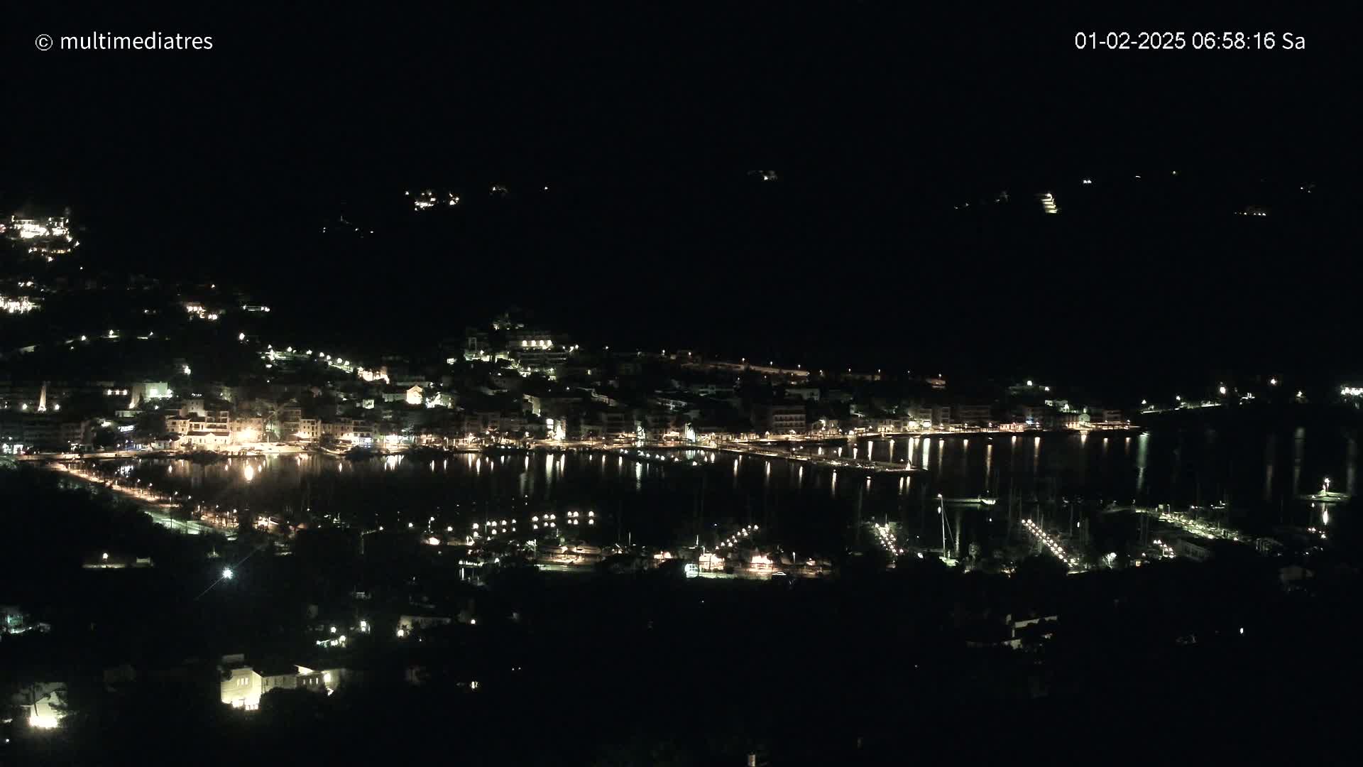 A nighttime view of a coastal town illuminated with lights, reflecting on a calm body of water.
