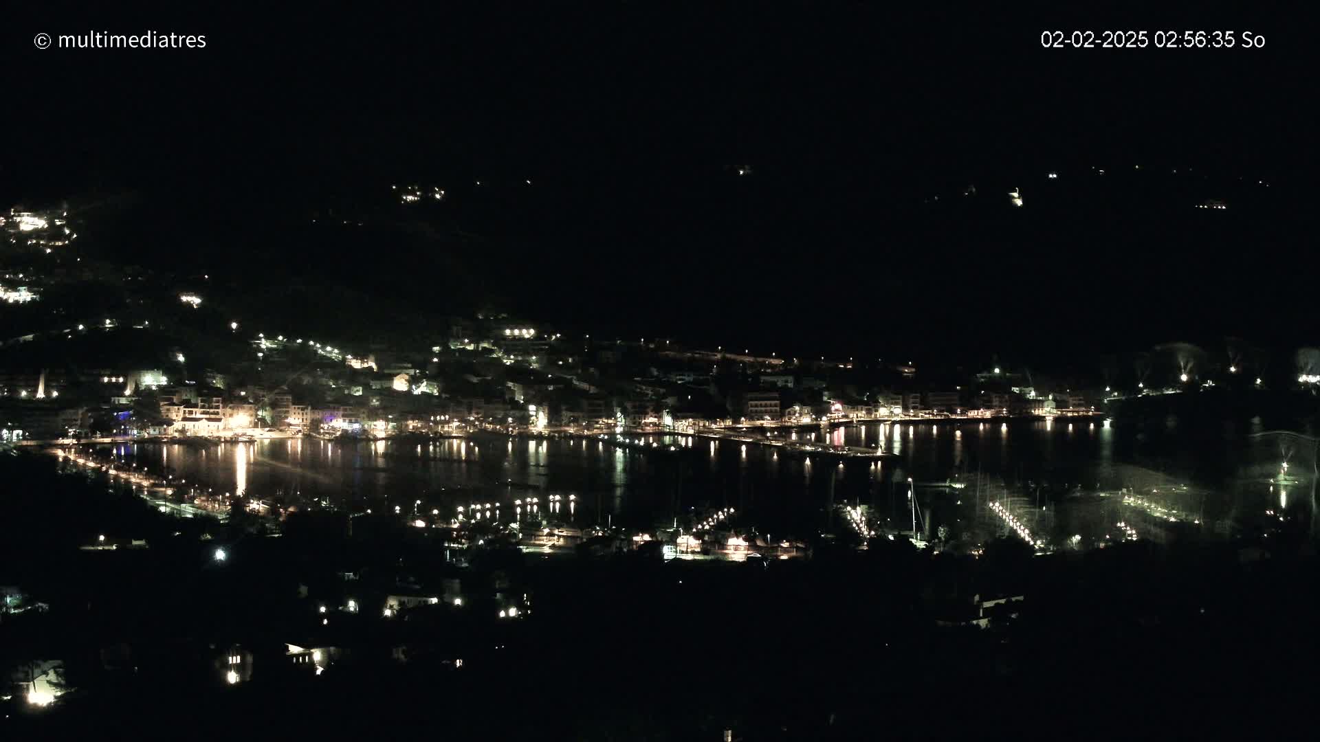 A nighttime view of a coastal town with its lights reflecting on a calm body of water.