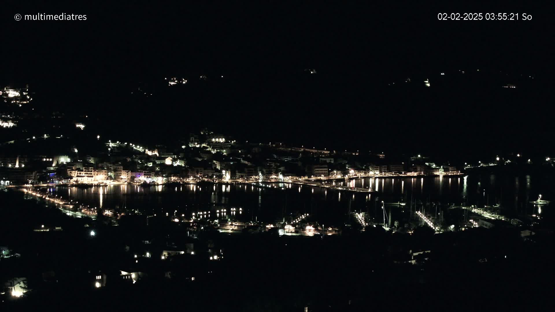 A nighttime view of a coastal town with its lights reflected in a calm body of water.