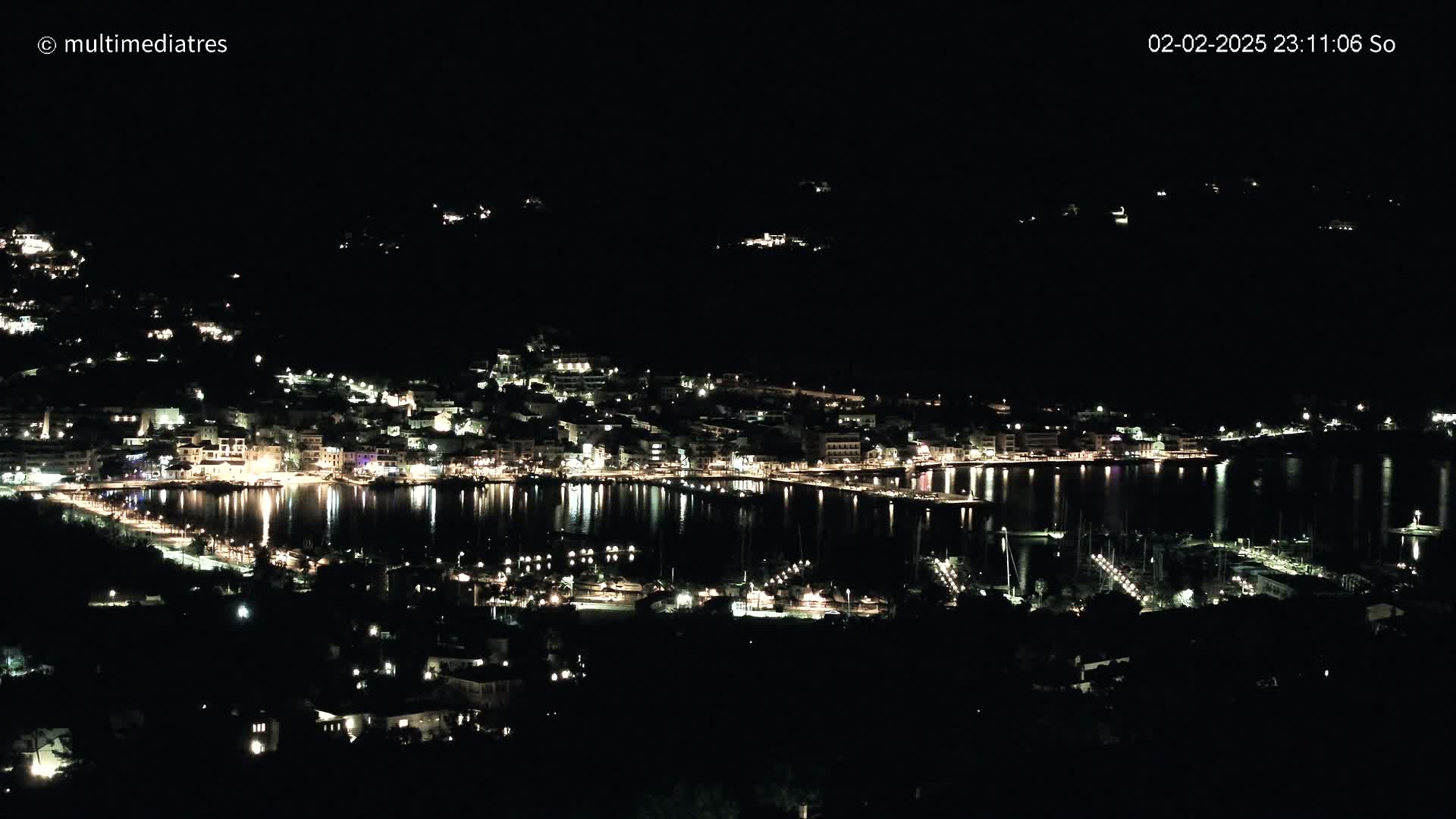 A nighttime view of a town situated on a body of water, with its lights reflecting on the still water's surface.
