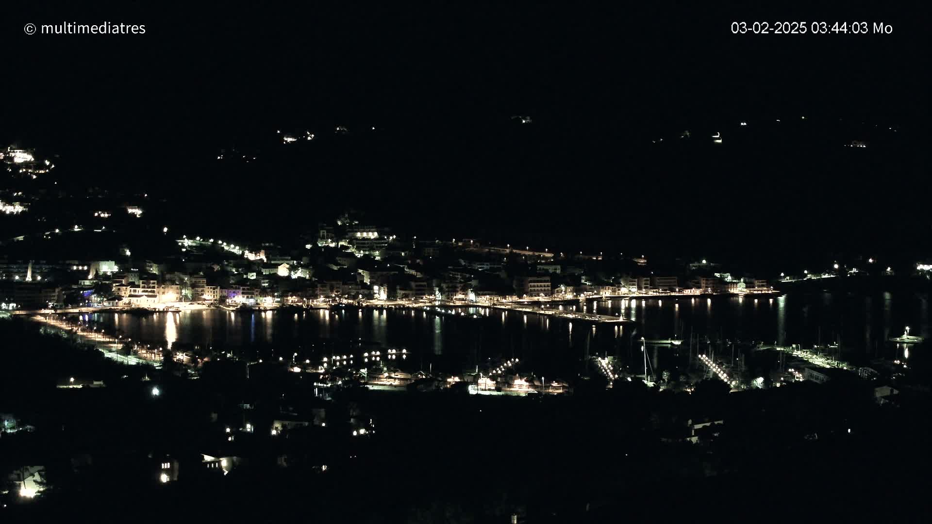 A nighttime view of a coastal town's lights illuminating the harbor and surrounding hillsides.