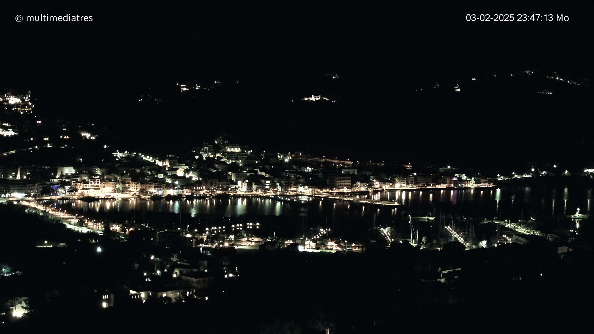 A coastal town at night, illuminated by many lights, is seen from a high vantage point under a clear, dark sky.