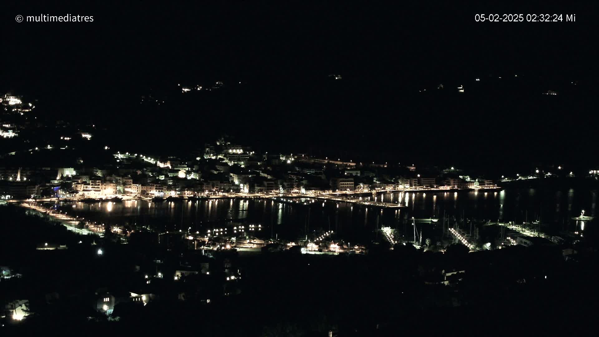 A nighttime view of a harbor town, with its lights reflecting on the calm water.