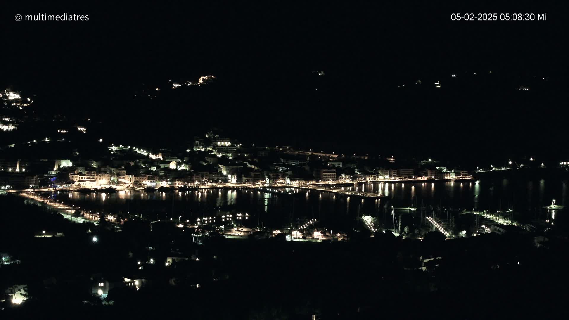 A nighttime view of a coastal town with its lights reflecting on the calm water of a harbor.