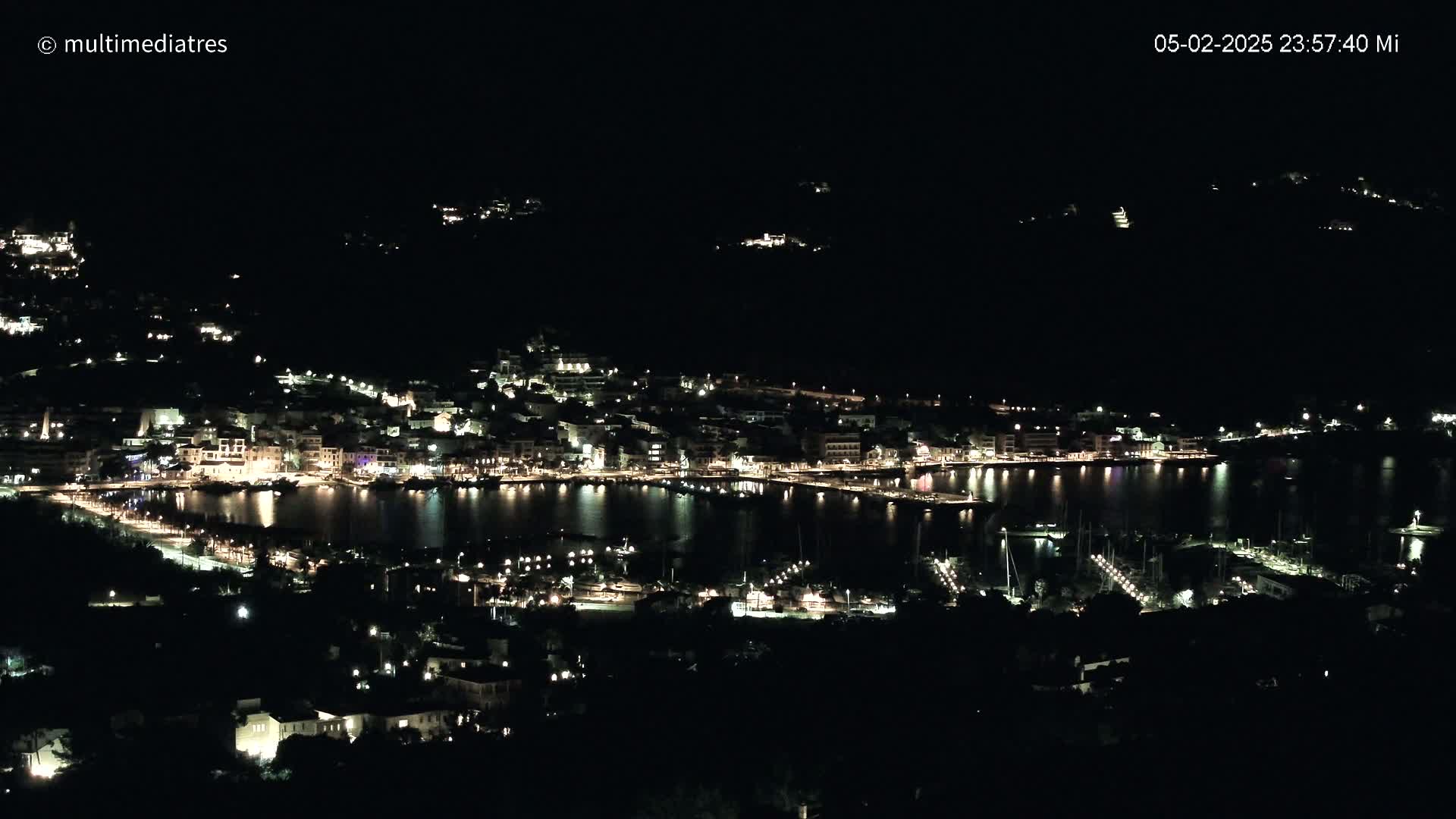A nighttime view of a coastal town with its lights illuminating the harbor and surrounding buildings.