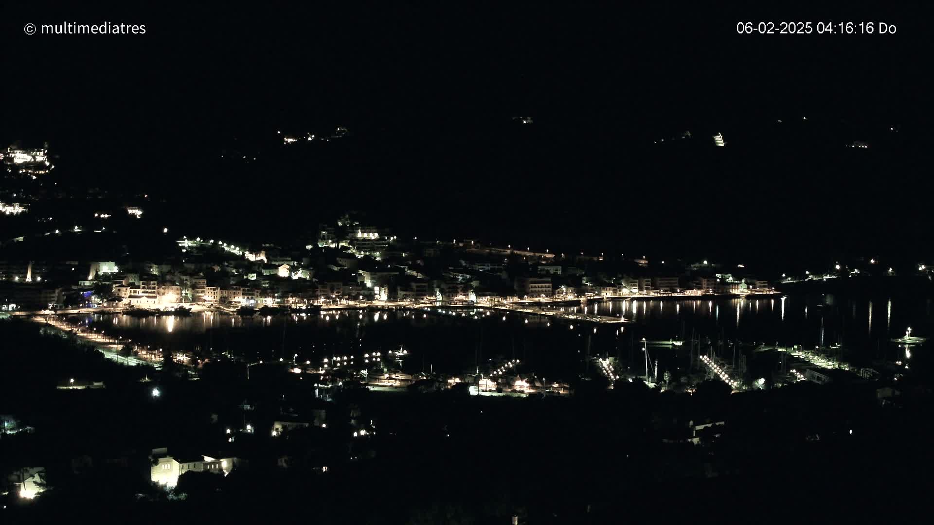 A nighttime view of a coastal town with its lights reflecting on the calm water of a harbor.