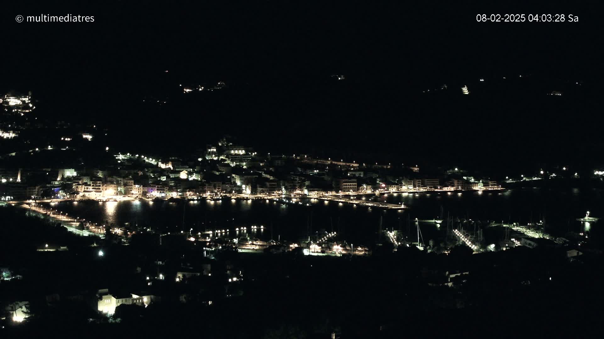 A coastal town at night, illuminated by many lights, is seen from a distance under a clear, dark sky.