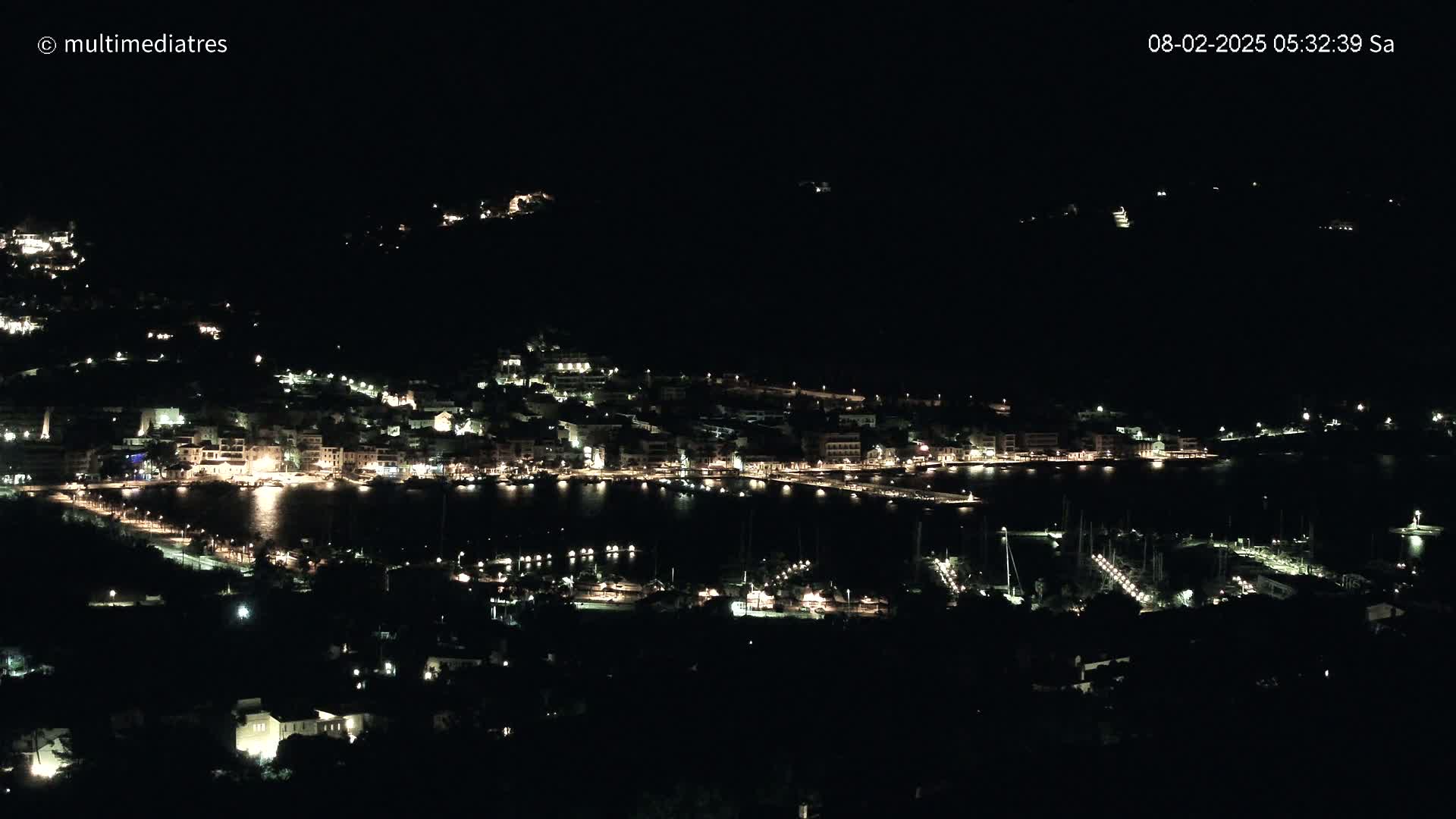A nighttime, aerial view of a coastal town with its lights illuminating the buildings and harbor.