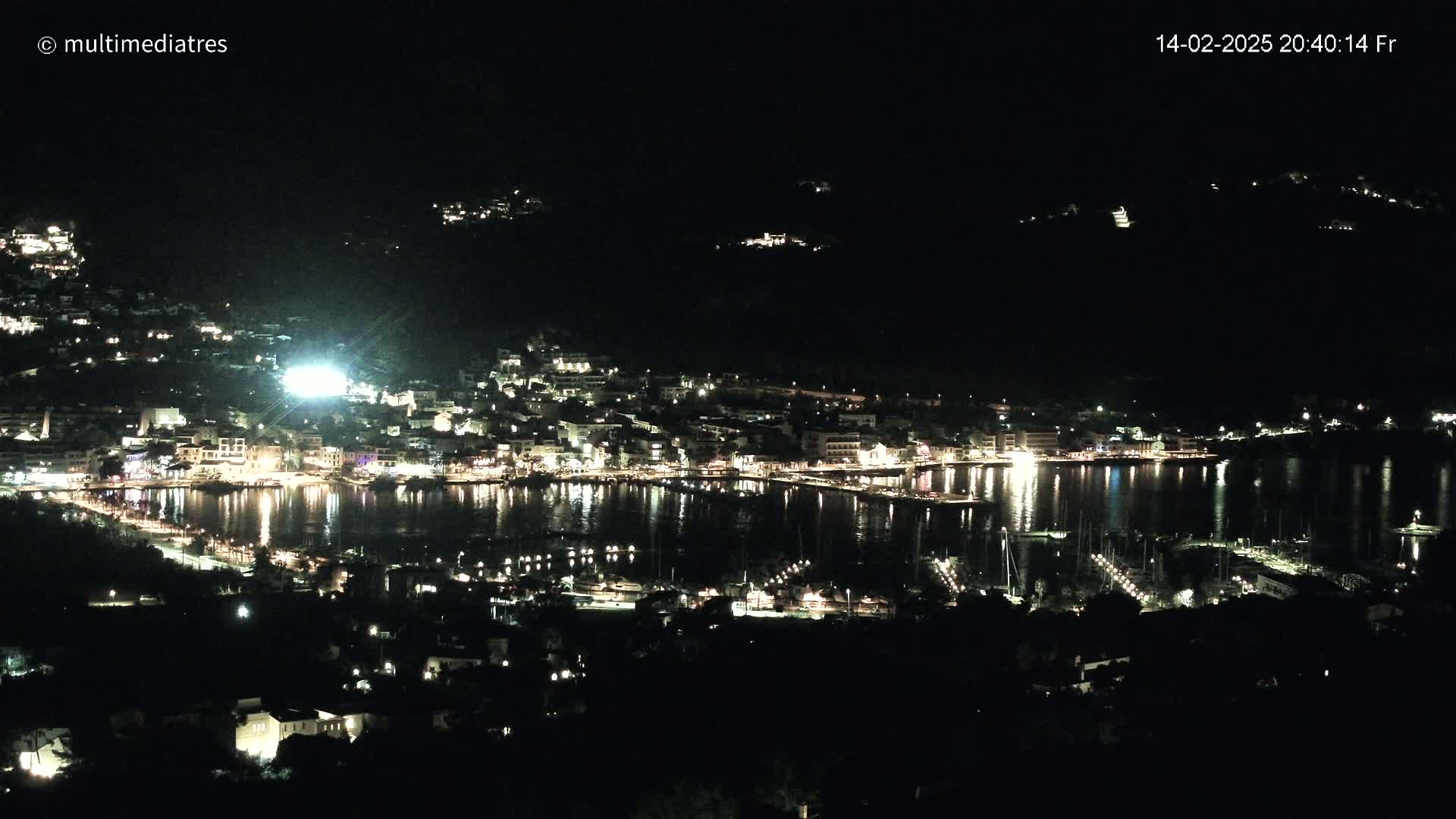 A nighttime view of a coastal town with its lights reflecting on a calm body of water.