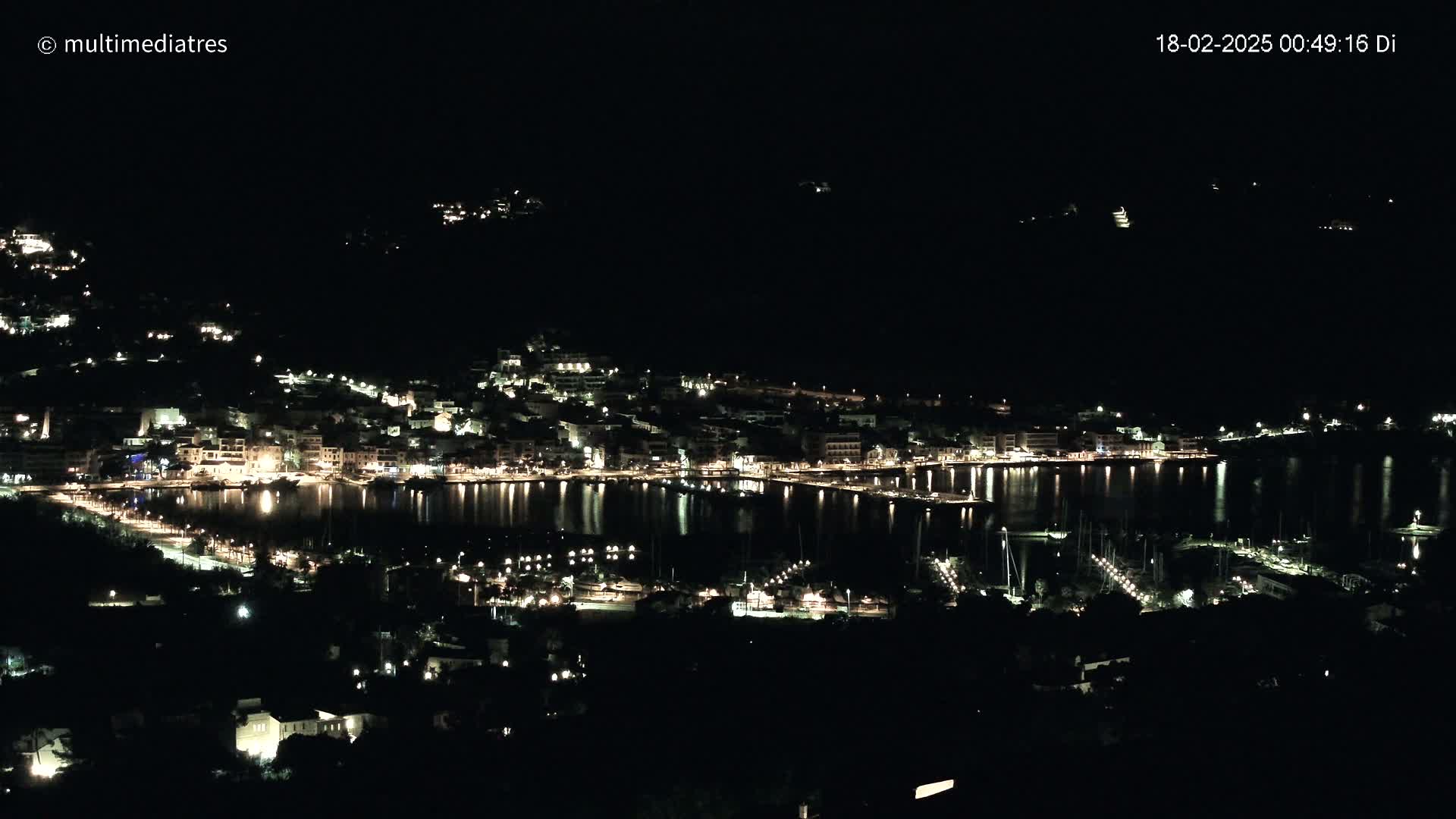 A nighttime view of a coastal town with its lights reflecting on calm water.