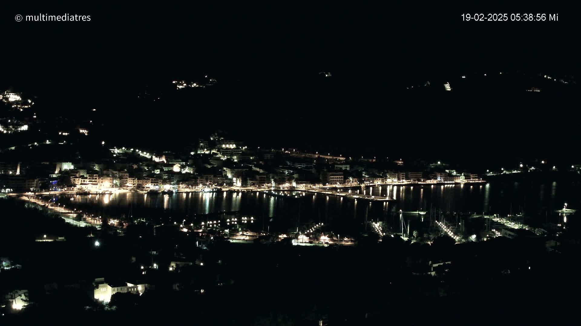 A nighttime view of a coastal town with its lights reflecting on a calm body of water.