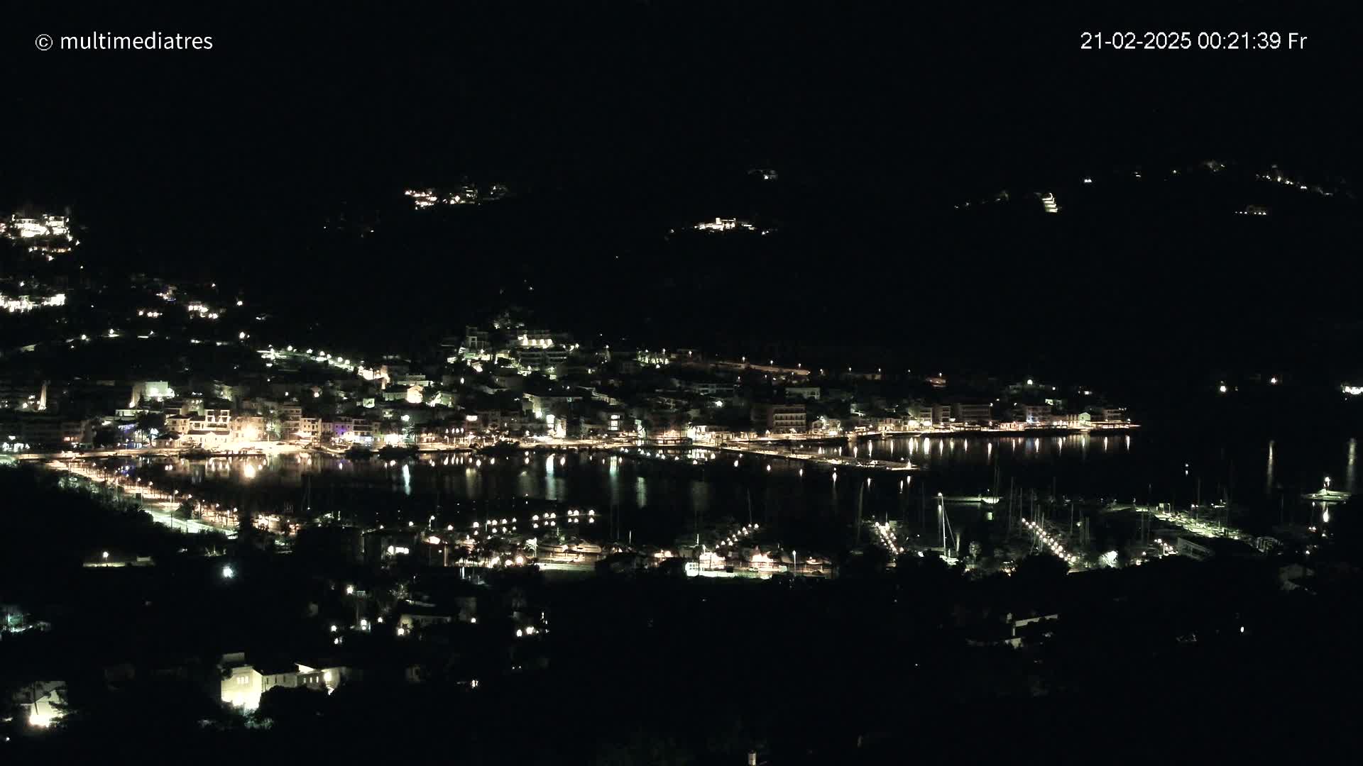 A nighttime view of a harbor town with many lights reflecting on the water under a clear, dark sky.