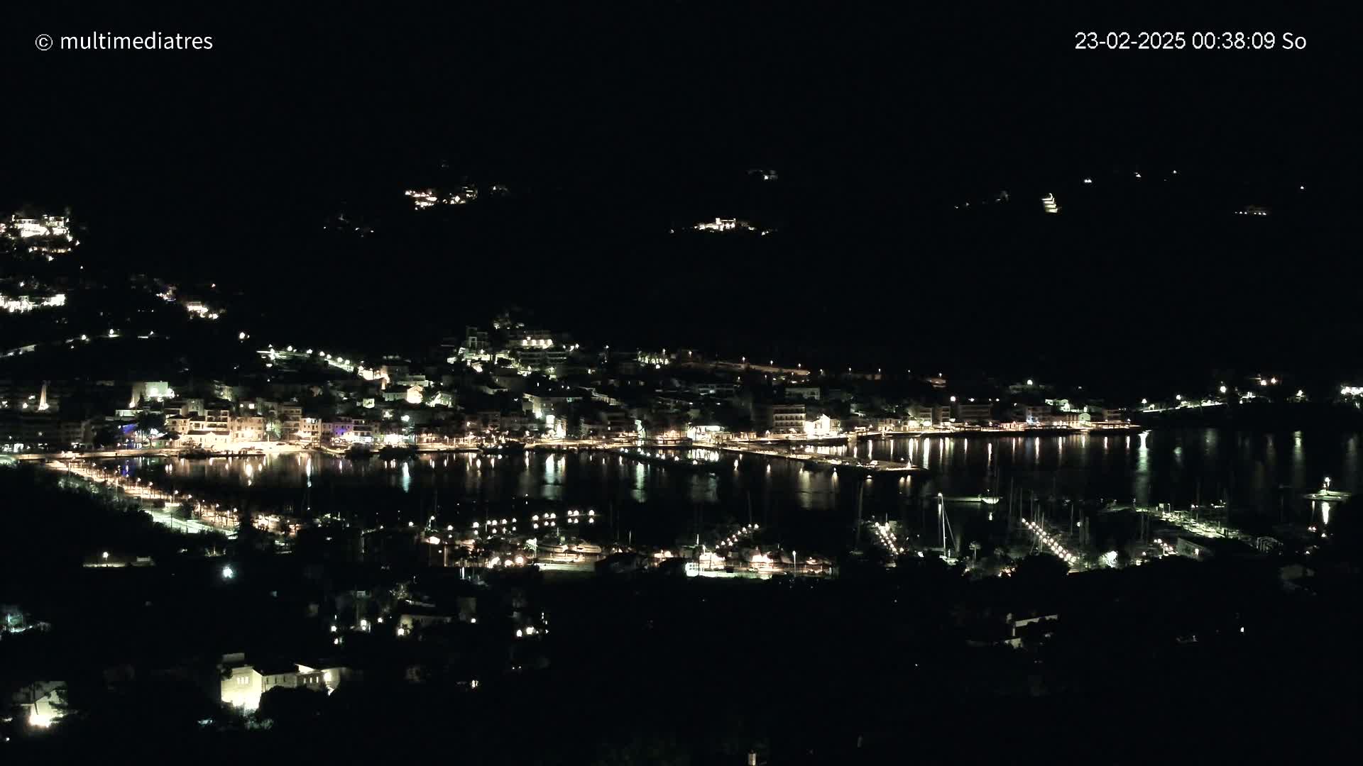 A nighttime, aerial view of a coastal town with its lights reflecting on a calm body of water.