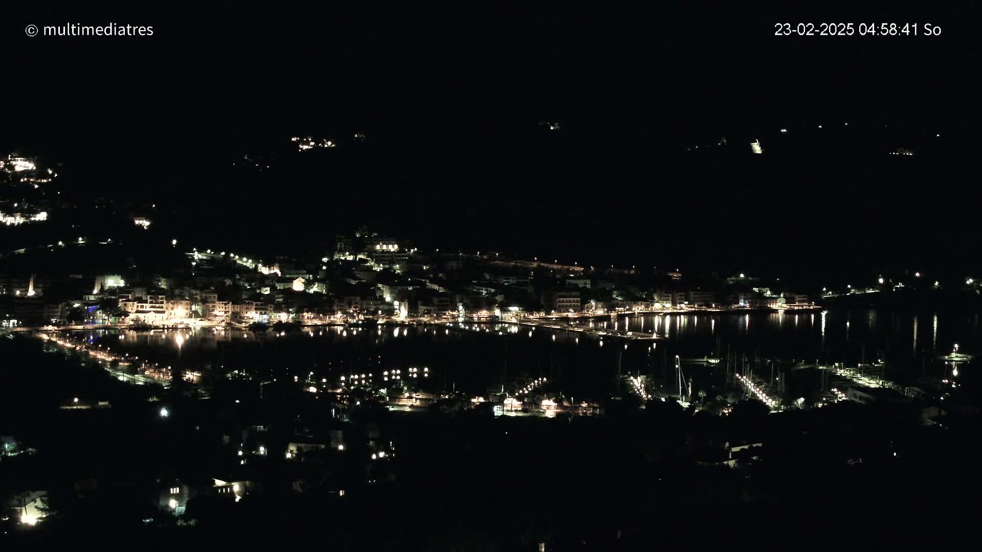 A coastal town at night, illuminated by lights reflecting on the calm water of a harbor.