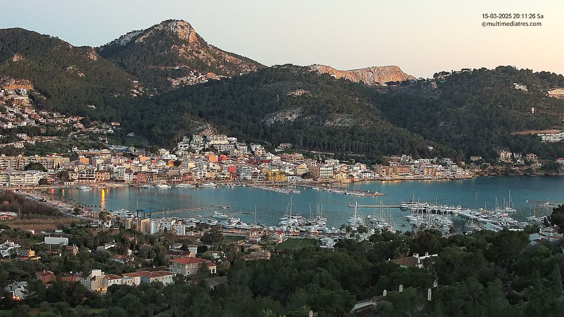 A coastal town nestled between hills at dusk, featuring a harbor filled with sailboats.
