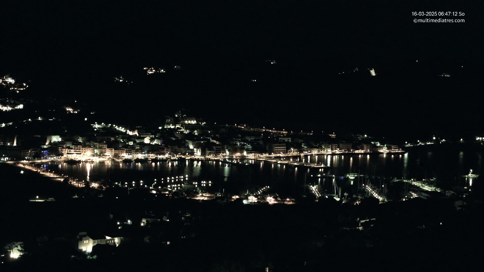 A nighttime view of a coastal town with its lights reflecting on a calm body of water.