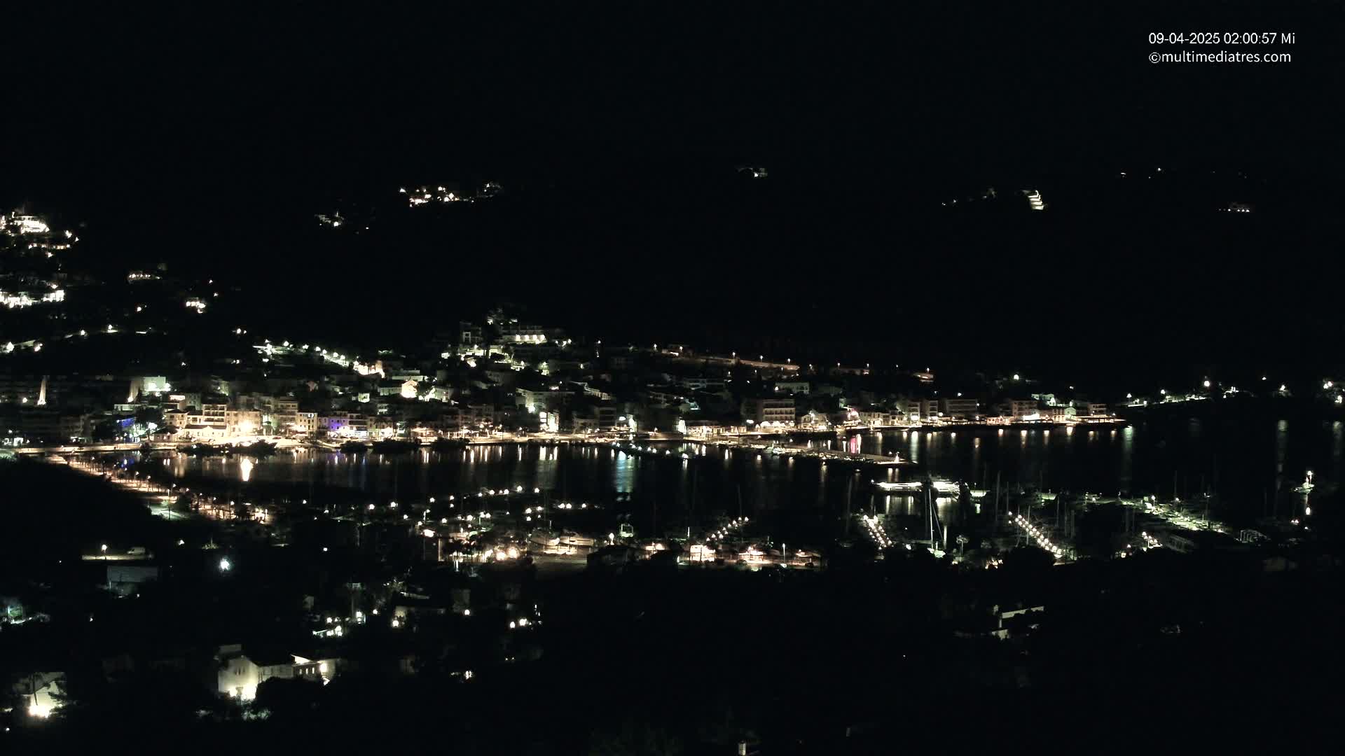 A coastal town at night, illuminated by lights reflecting on the calm water of a harbor.