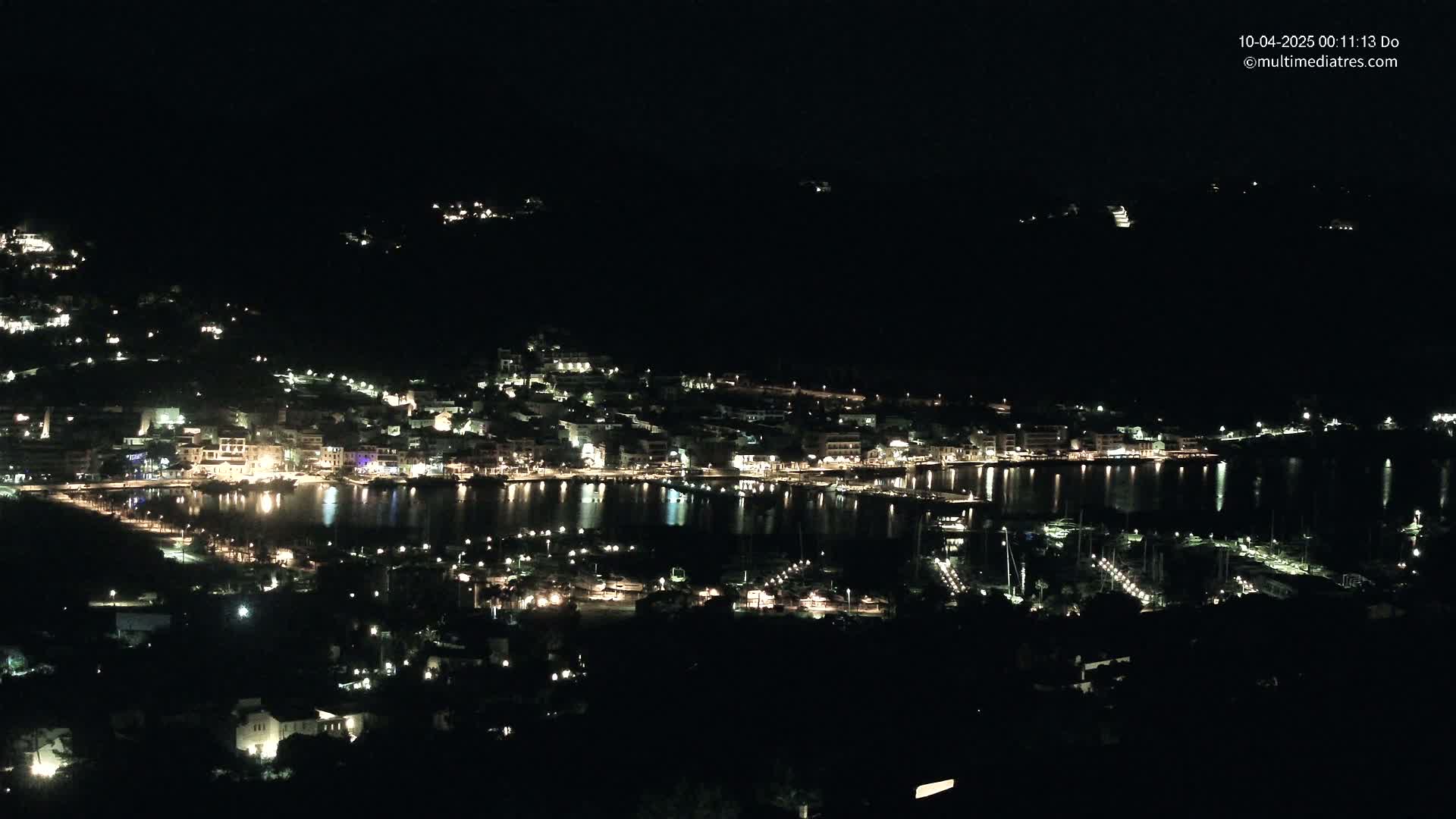 A nighttime, aerial view of a coastal town with its lights reflecting on a calm body of water.