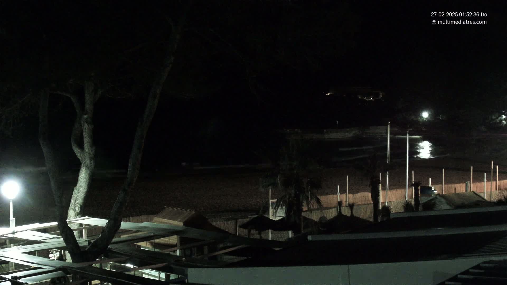 A nighttime view of a dark beach with structures and palm trees, under a clear sky.