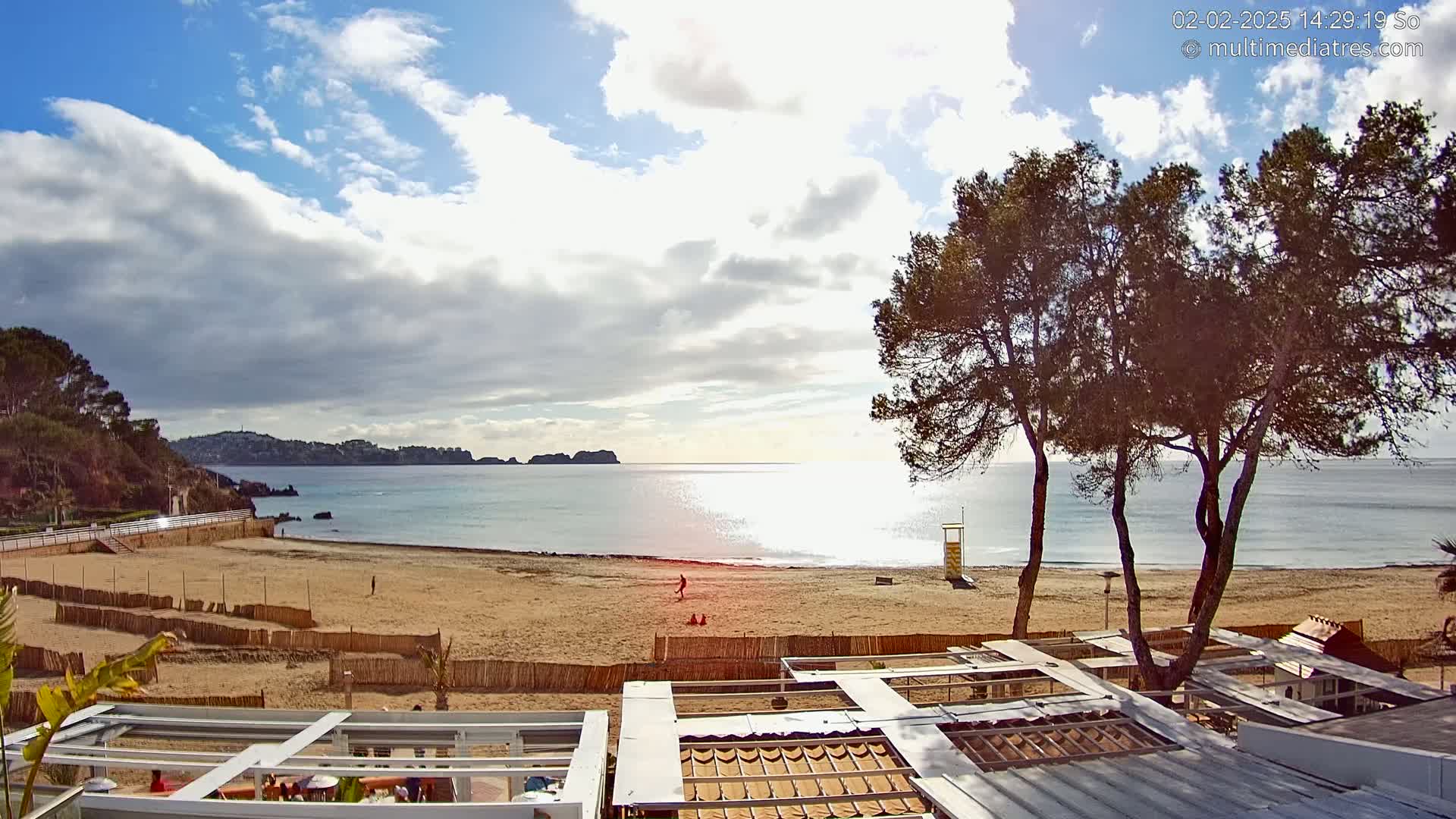 A sandy beach with calm, clear water under a partly cloudy sky, viewed from above a beachside structure.