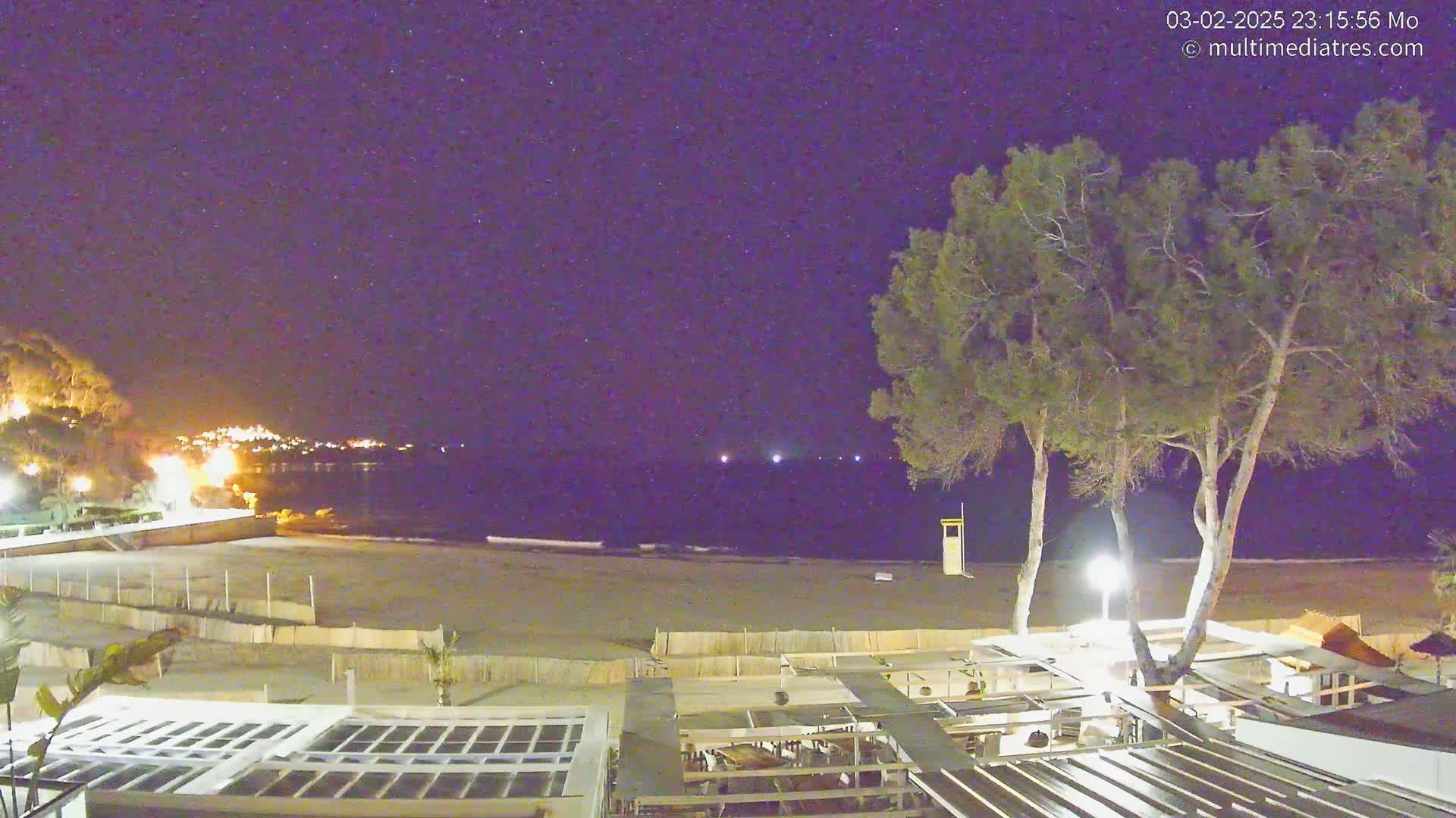 A nighttime view of a beach with a restaurant and trees under a clear, starry sky.