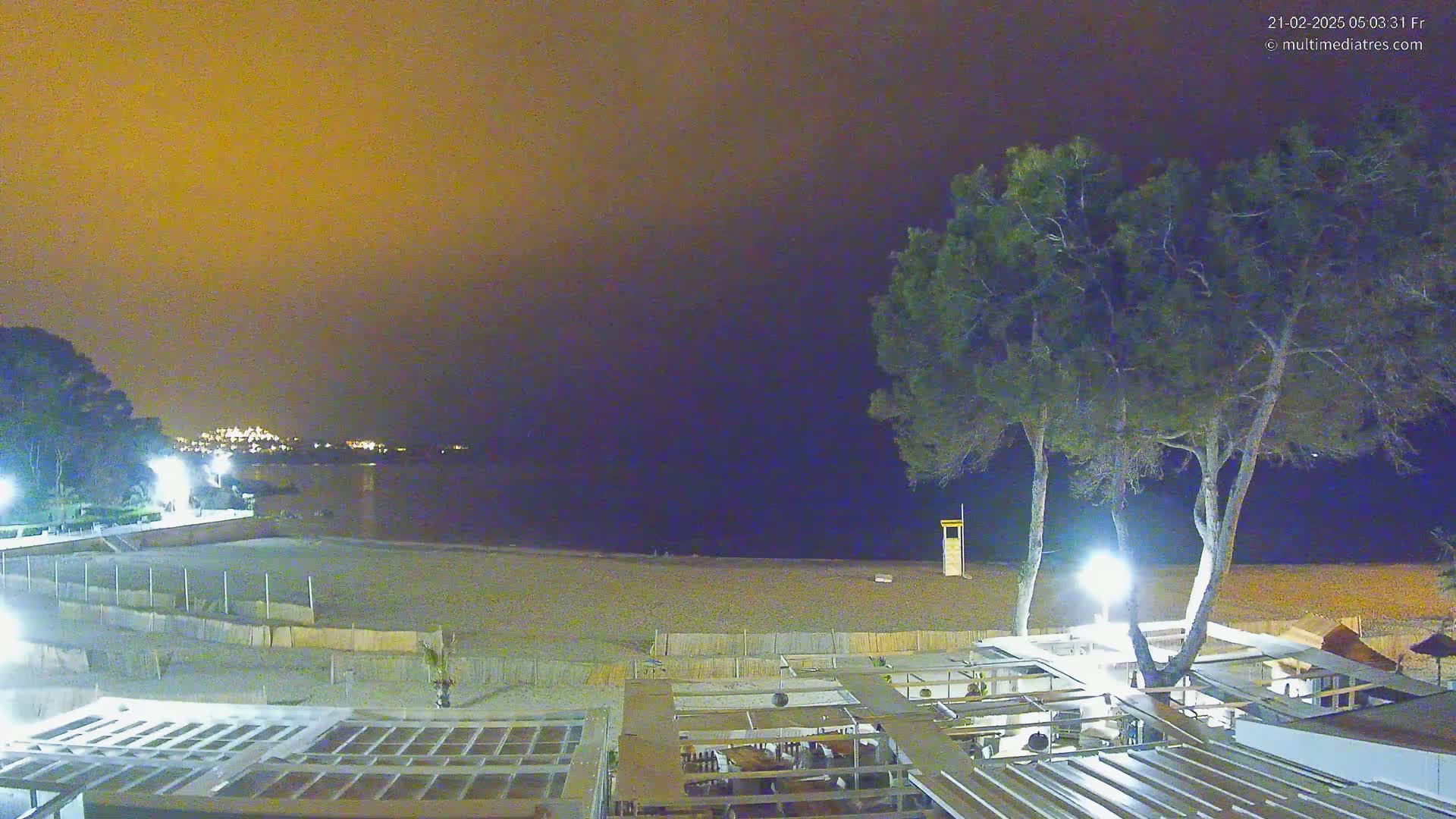 A nighttime view of a beach with a restaurant and trees under an orange-tinged sky.