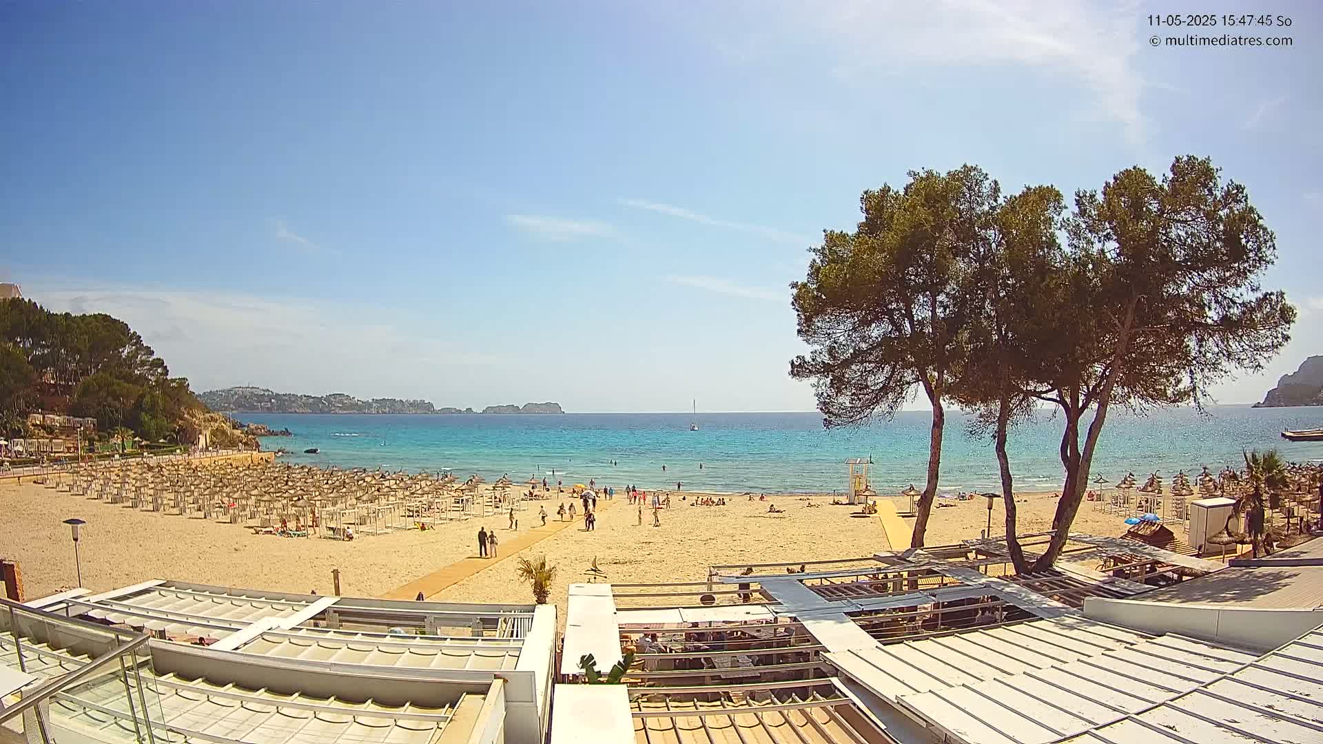 A sandy beach with many umbrellas and people, situated beside a calm, turquoise ocean under a clear blue sky.