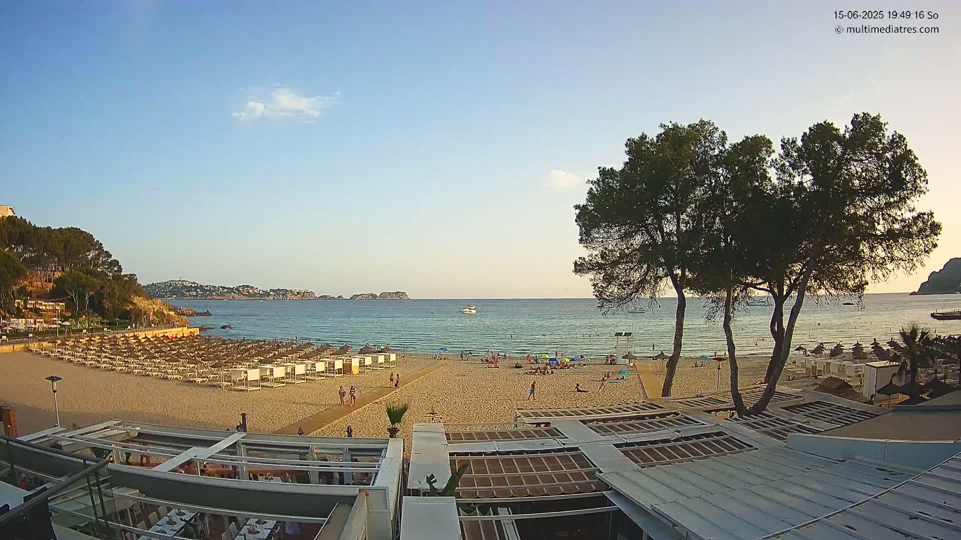A sandy beach with many beach umbrellas and a few people is visible, with calm water and a clear sky in the background.