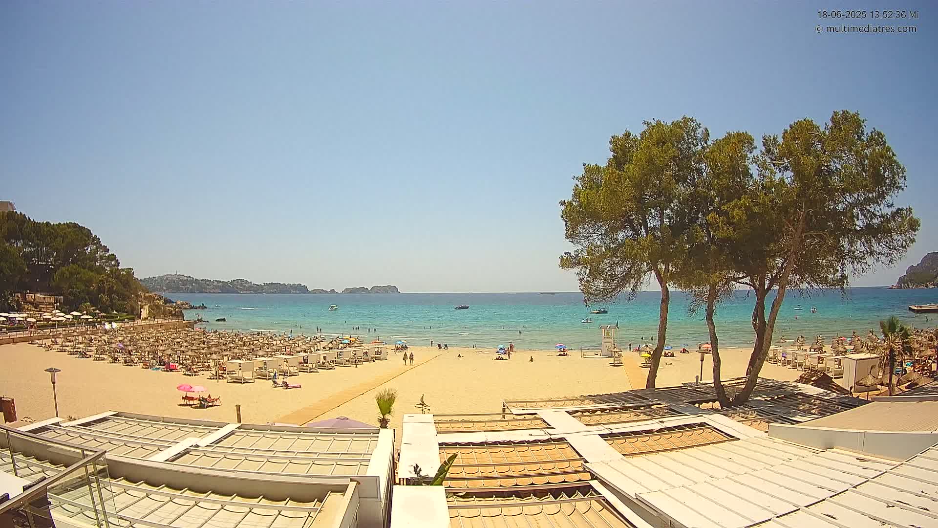A sandy beach with numerous lounge chairs and umbrellas under a clear, sunny sky, overlooks a calm, turquoise ocean.