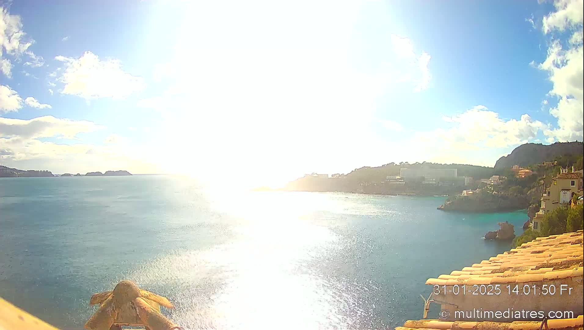 A sunny day overlooking a calm sea with distant islands and a coastline featuring buildings and vegetation.
