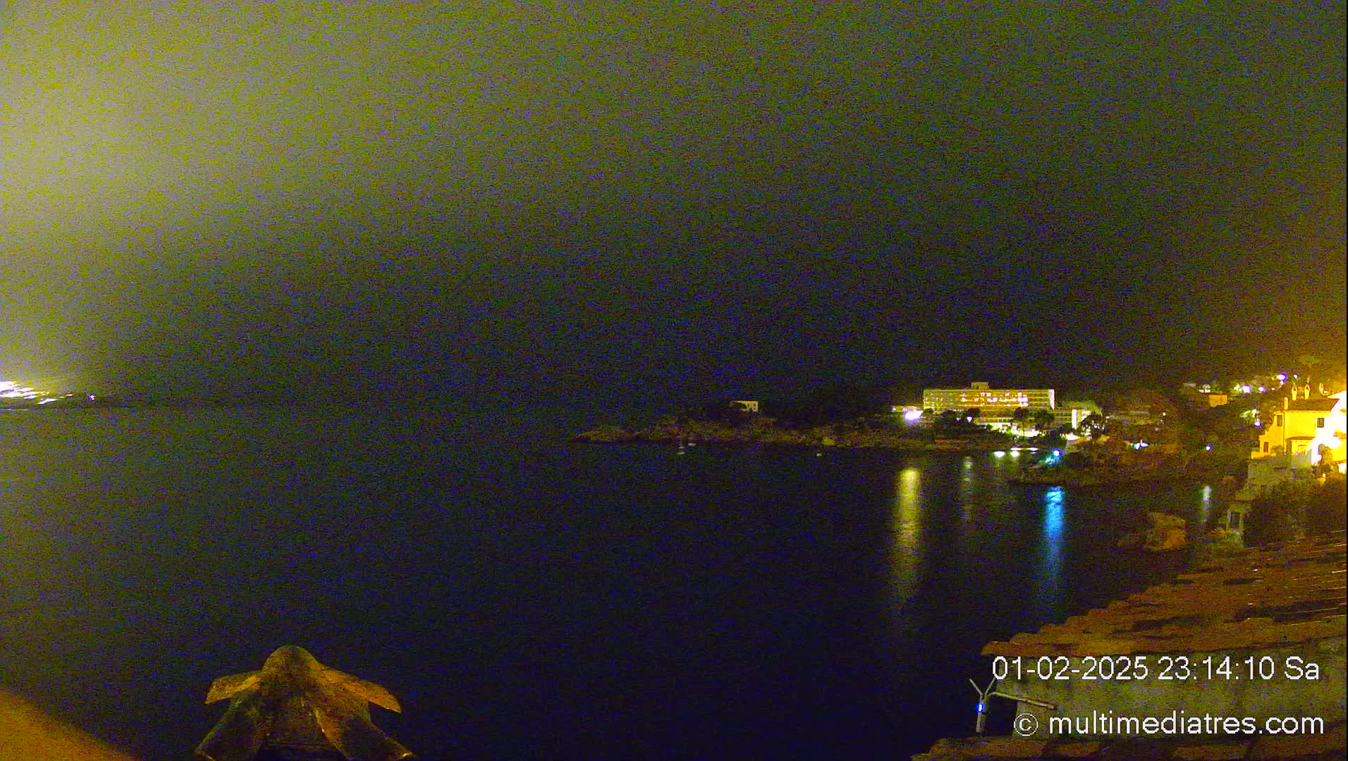 A nighttime view of a calm body of water with illuminated buildings and a hazy sky.
