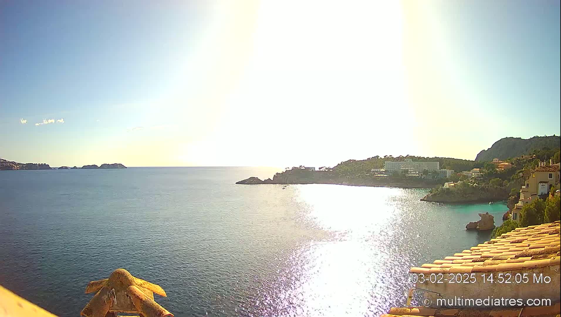 A sunny day overlooking a calm sea with a coastline featuring buildings and rocky outcrops.