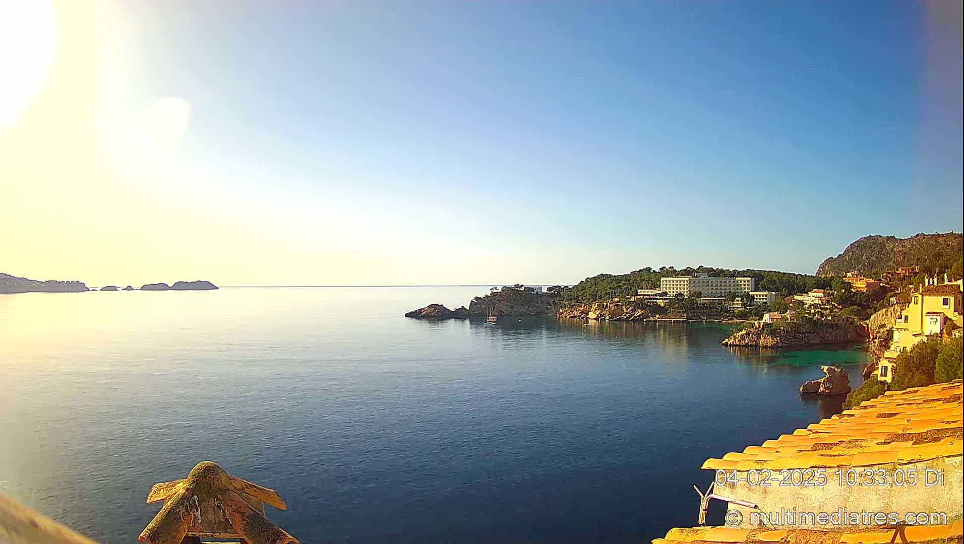 A tranquil ocean cove with a hotel and residential buildings nestled on a rocky hillside under a clear, sunny sky.